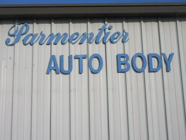 Sign on the side of a building that reads 'Parmentier Auto Body' in blue letters.