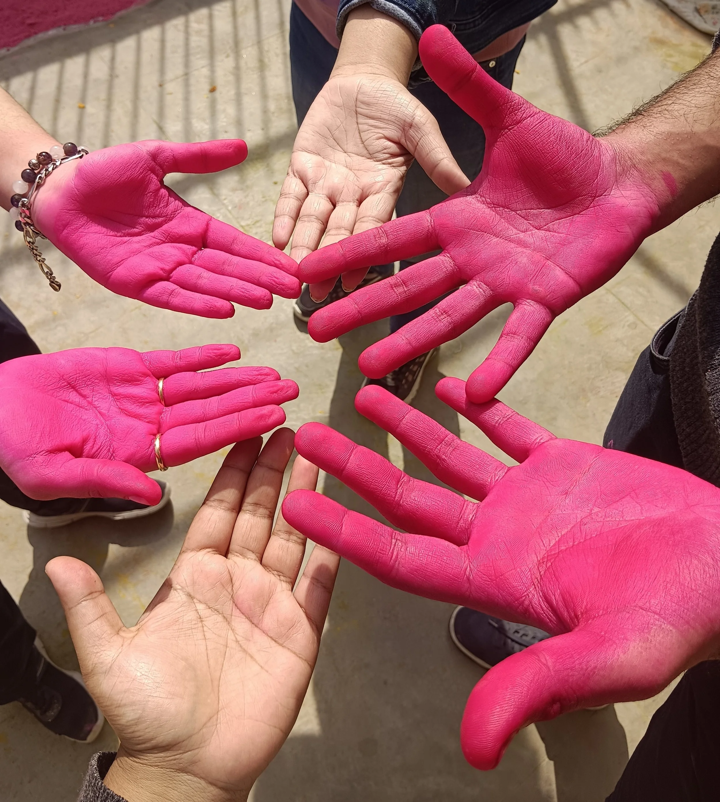 Multiple hands, some wearing pink gloves, come together in a heart shape, symbolizing connection and unity.