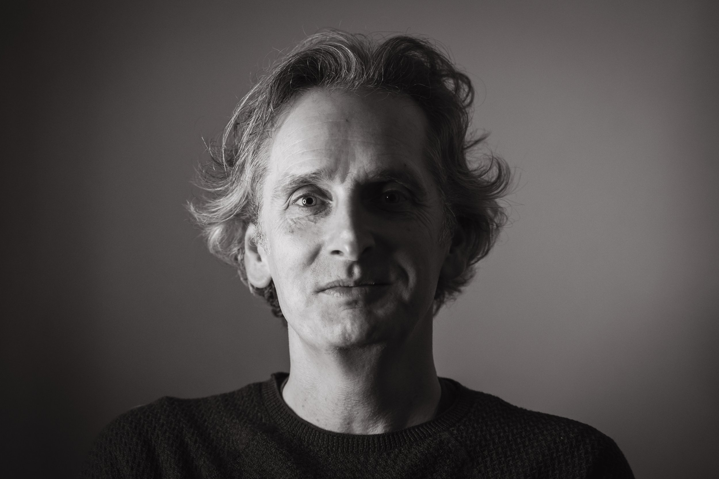 Black and white portrait of a man with short, curly hair, wearing a dark sweater, against a plain background.
