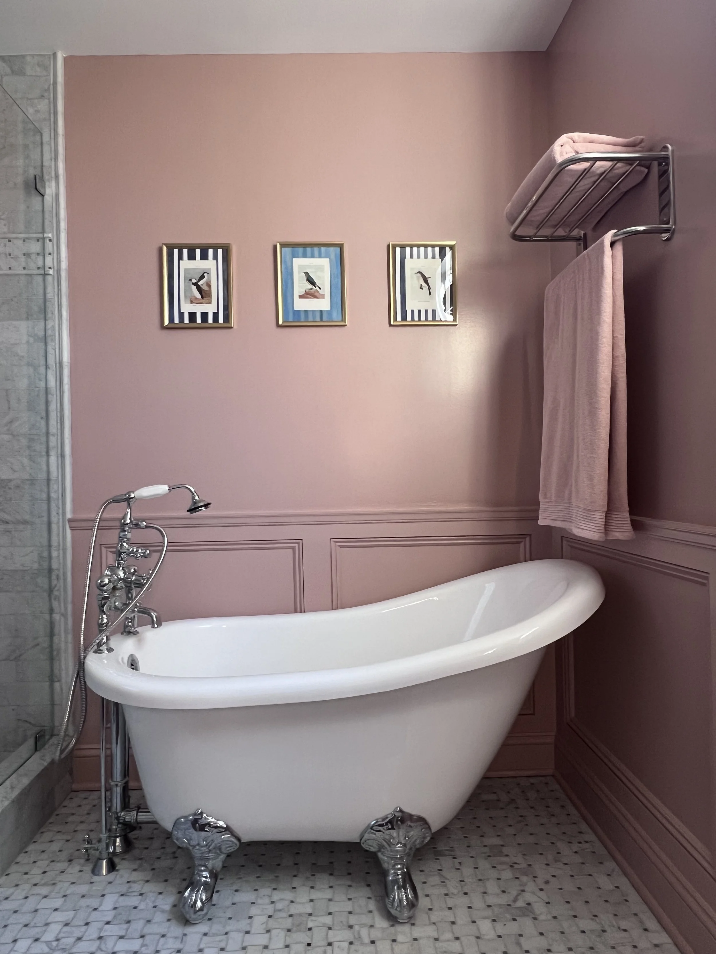A vintage-style freestanding clawfoot bathtub with chrome fixtures and four ornate clawfoot legs, against a pink wall decorated with three custom framed bird illustrations.