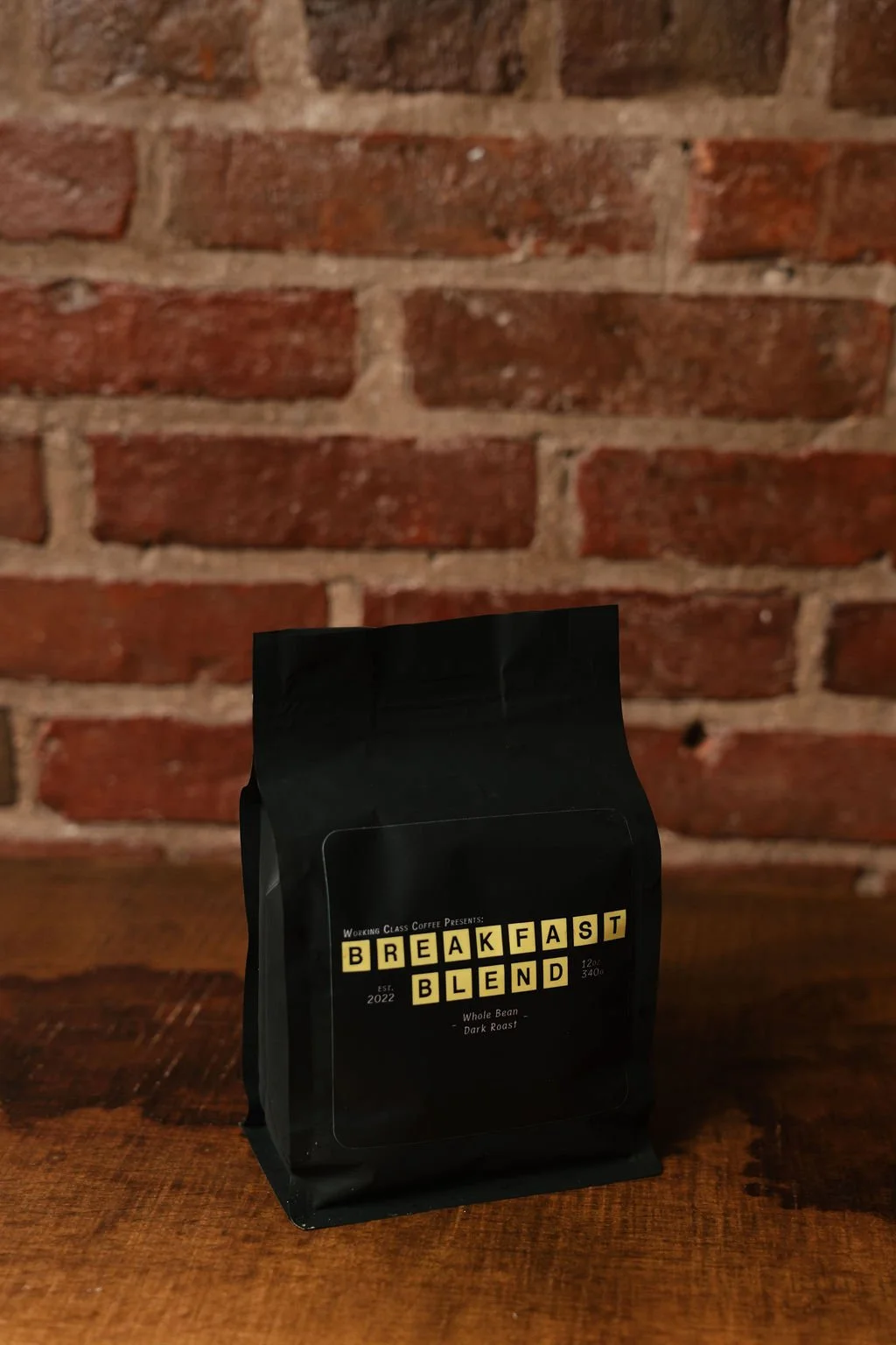 Black bag of coffee labeled 'Breakfast Blend' on a wooden table with a brick wall background.