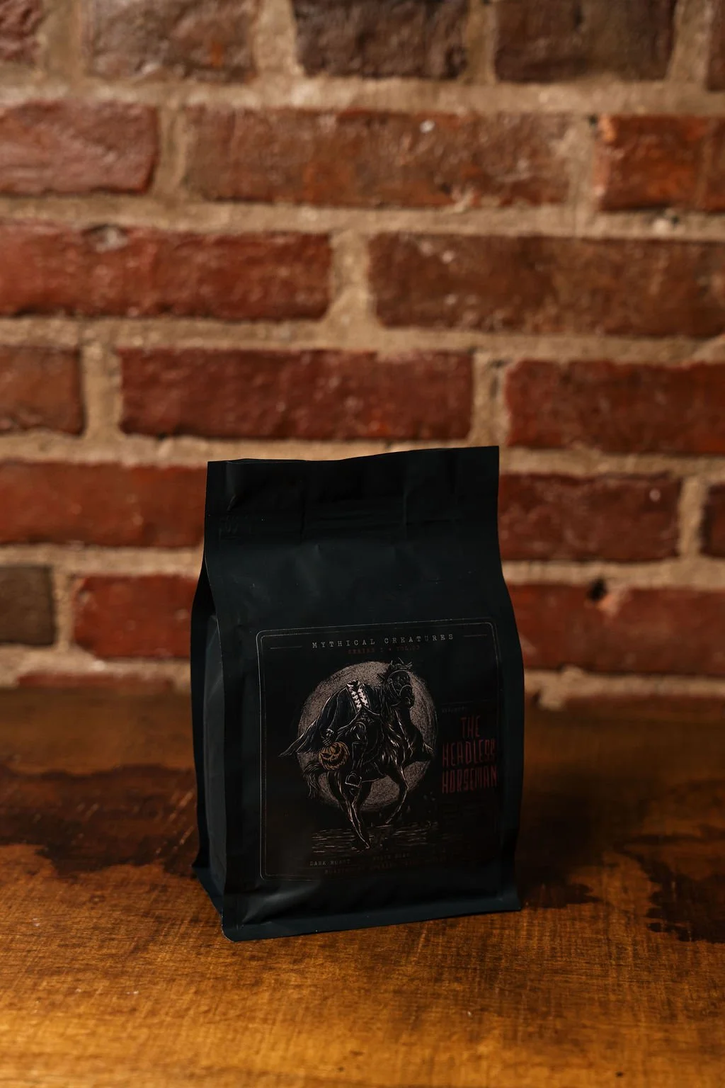 A black coffee bag with a label featuring an illustration of a horse and rider, against a brick wall background.