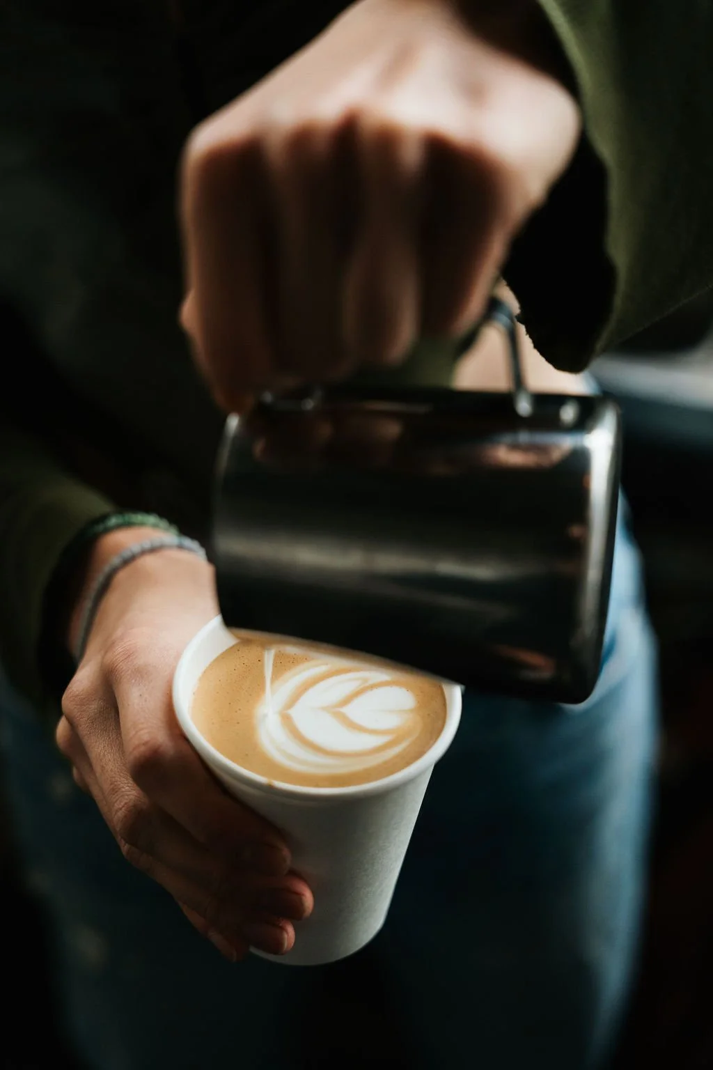 Person pouring steamed milk into a cup of coffee with latte art.