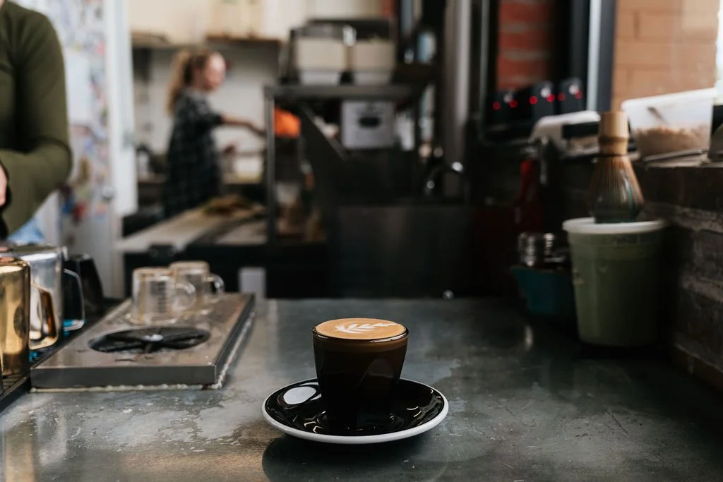 A cup of coffee with latte art on a saucer sitting on a counter in a coffee shop.