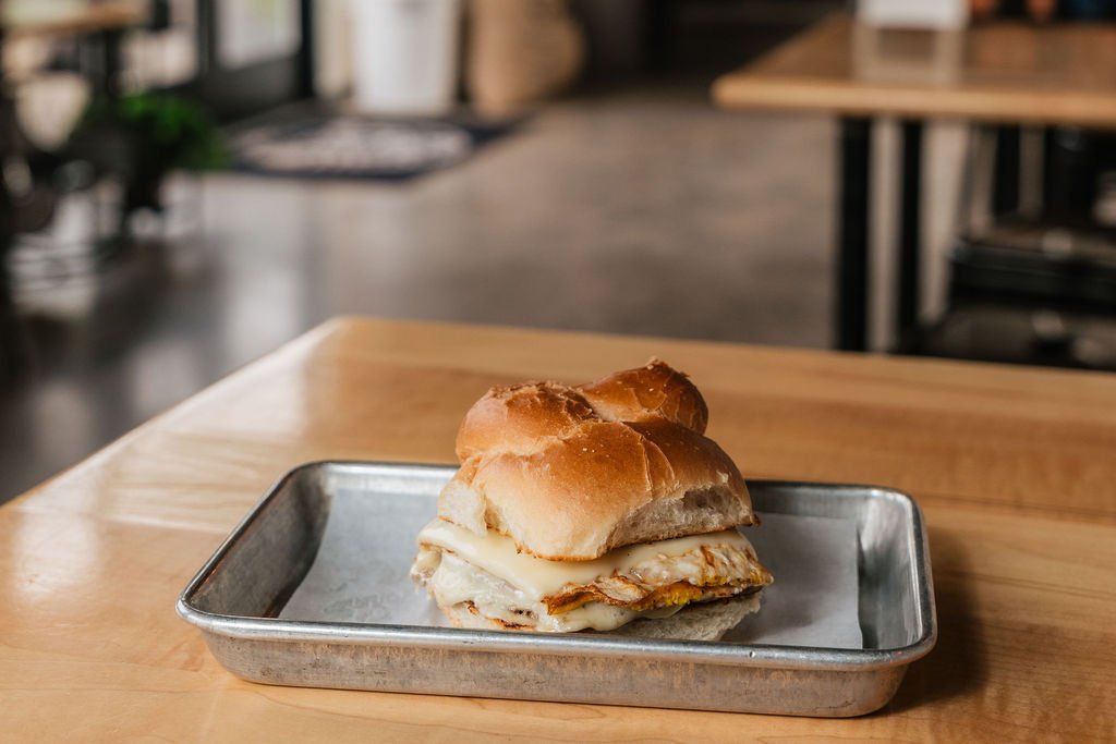 Egg and cheese breakfast sandwich on a toasted bun placed on a metal tray on a wooden table.