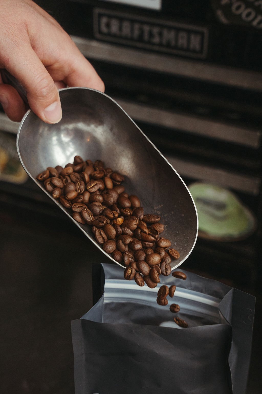 Close-up of a person pouring roasted coffee beans from a metal scoop into a bag.