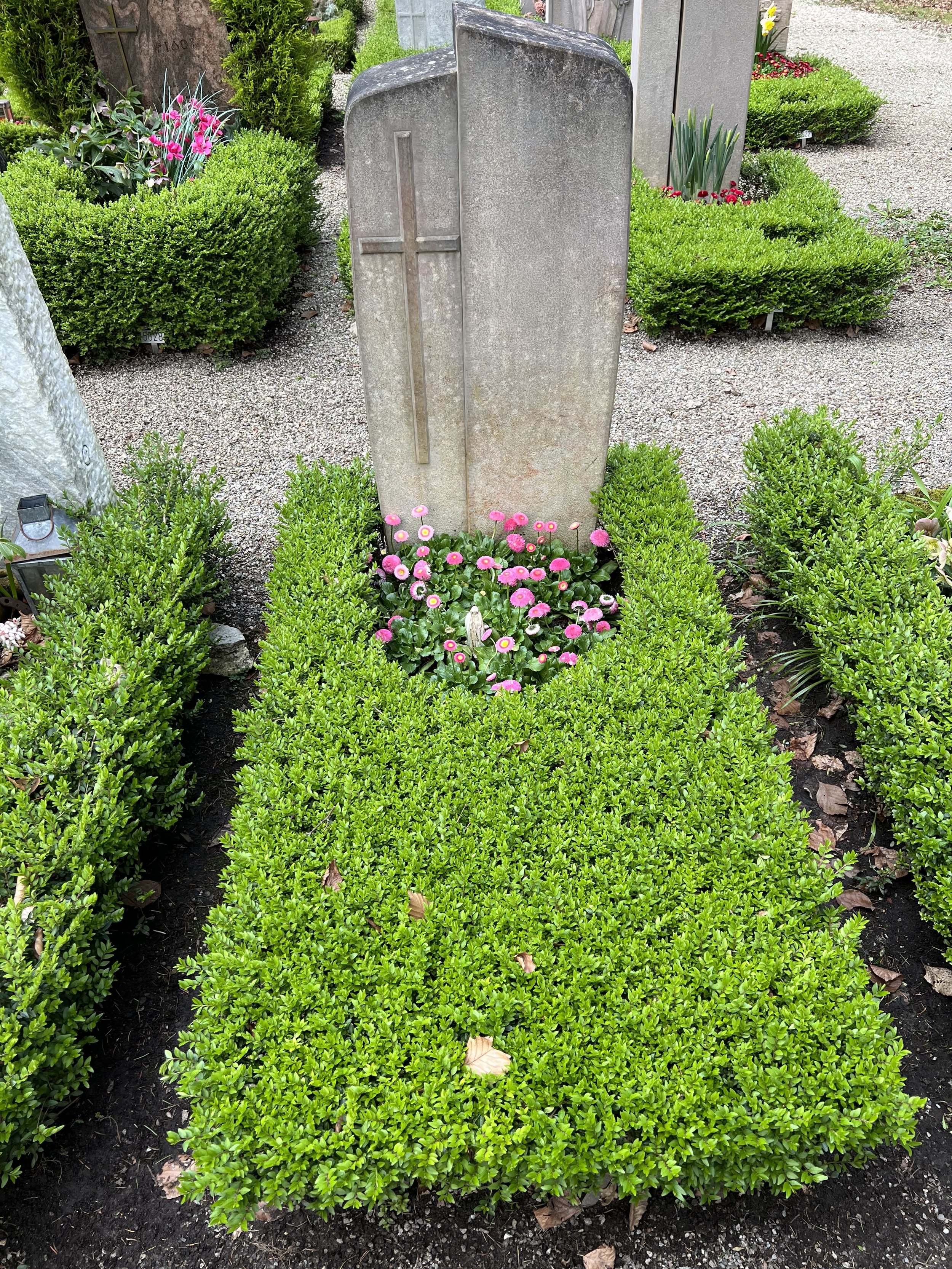 Grüner Garten mit Blumen und Grabsteinen auf einem Friedhof