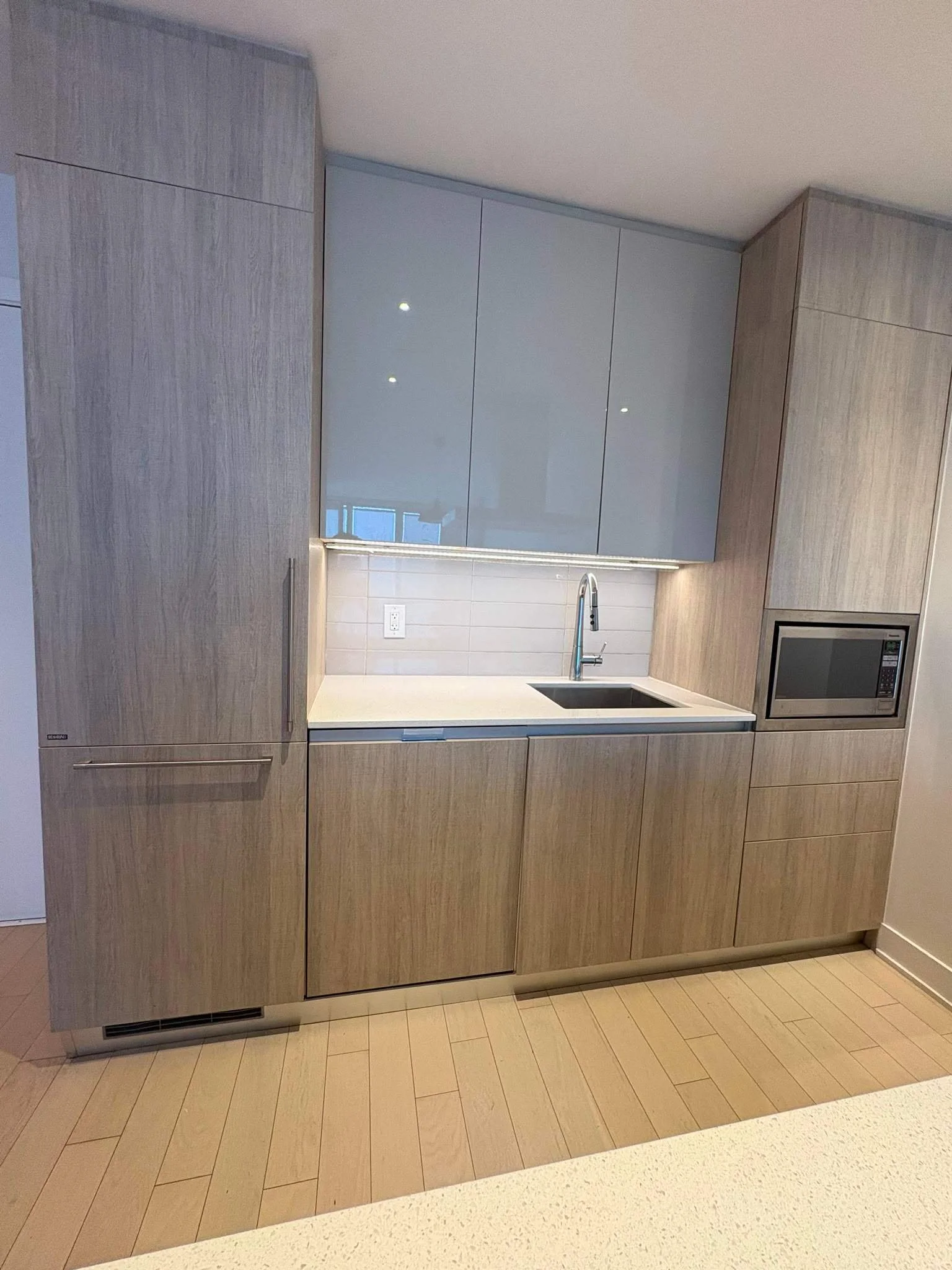 Modern kitchen with light wood cabinets, white countertops, a black sink, and a built-in microwave.