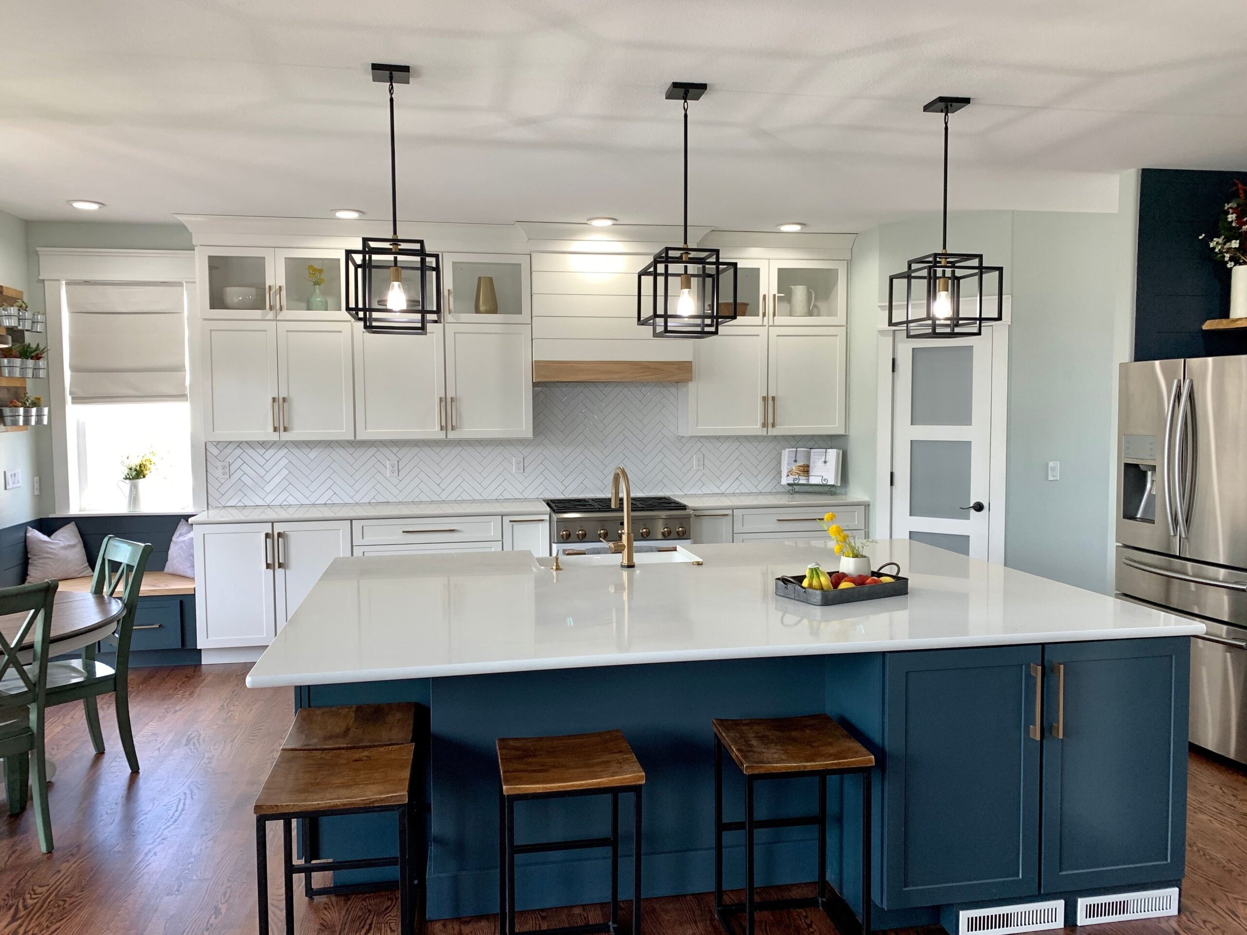 Modern kitchen with white cabinets, a large white island, black pendant lights, stainless steel refrigerator, and wooden stools.