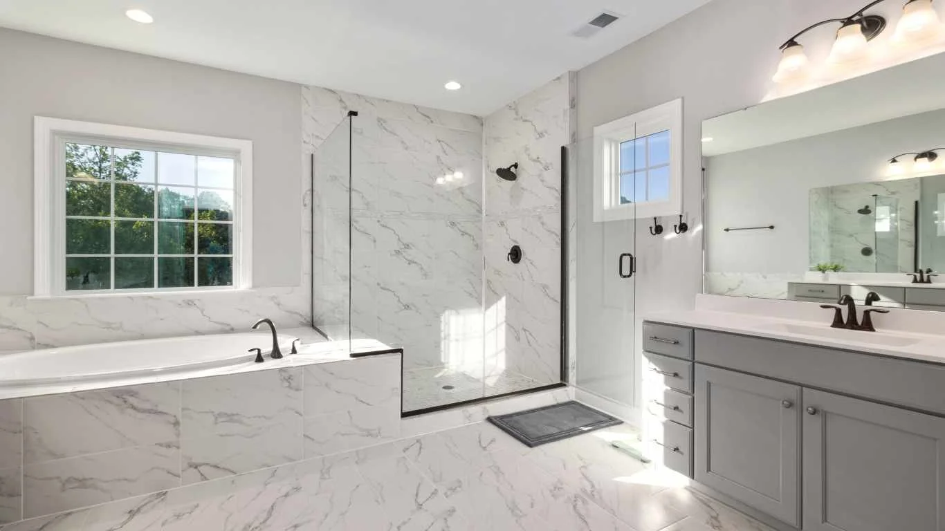 Modern bathroom with marble tiles, a bathtub under a window, a glass-enclosed shower, and a vanity with a mirror.