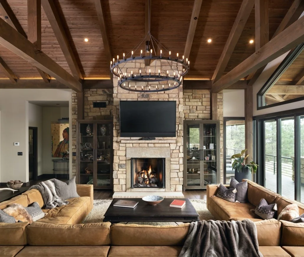 Living room with a stone fireplace, flat-screen TV, wooden ceiling, large windows, and leather sofa.