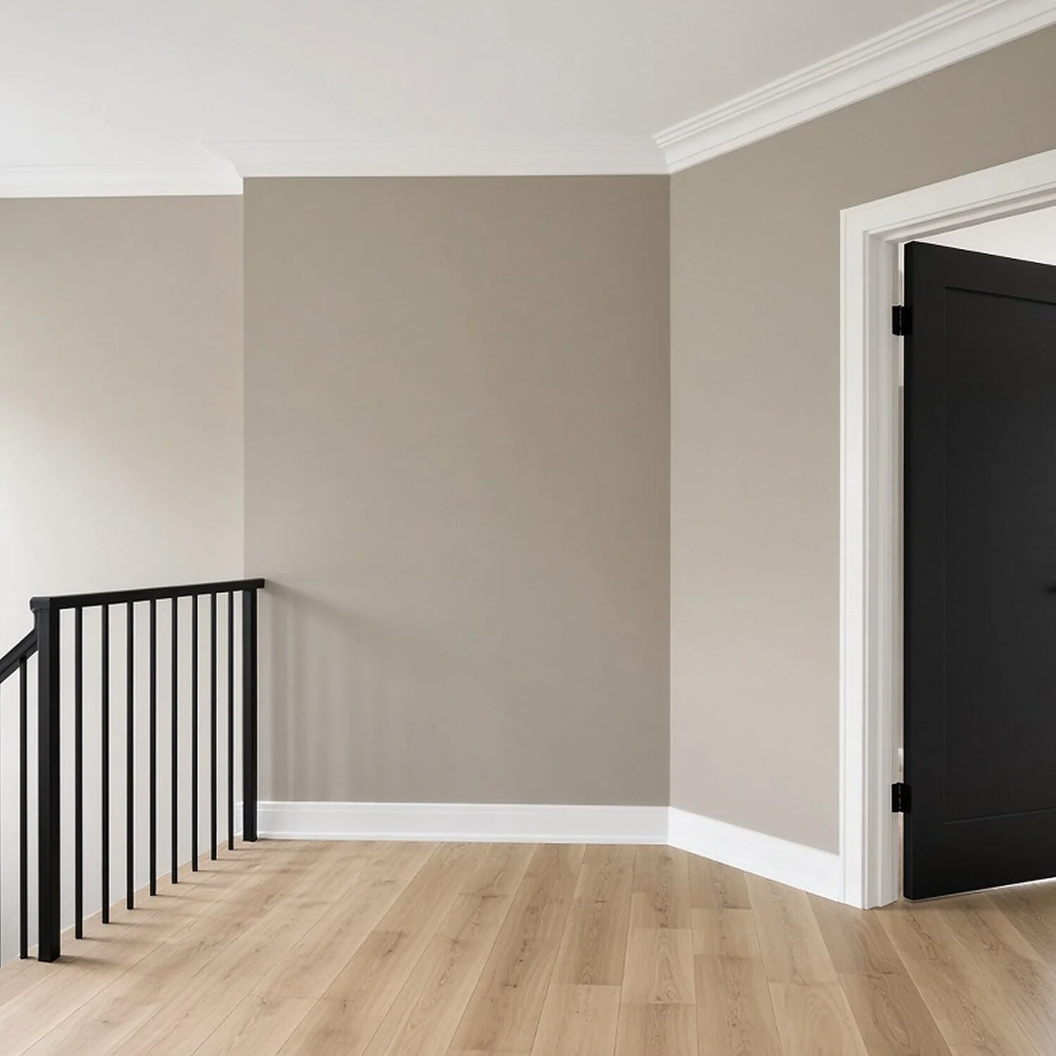 Interior corner of a house with beige walls, white crown molding, a black door partially open, hardwood flooring, and a black metal staircase railing.