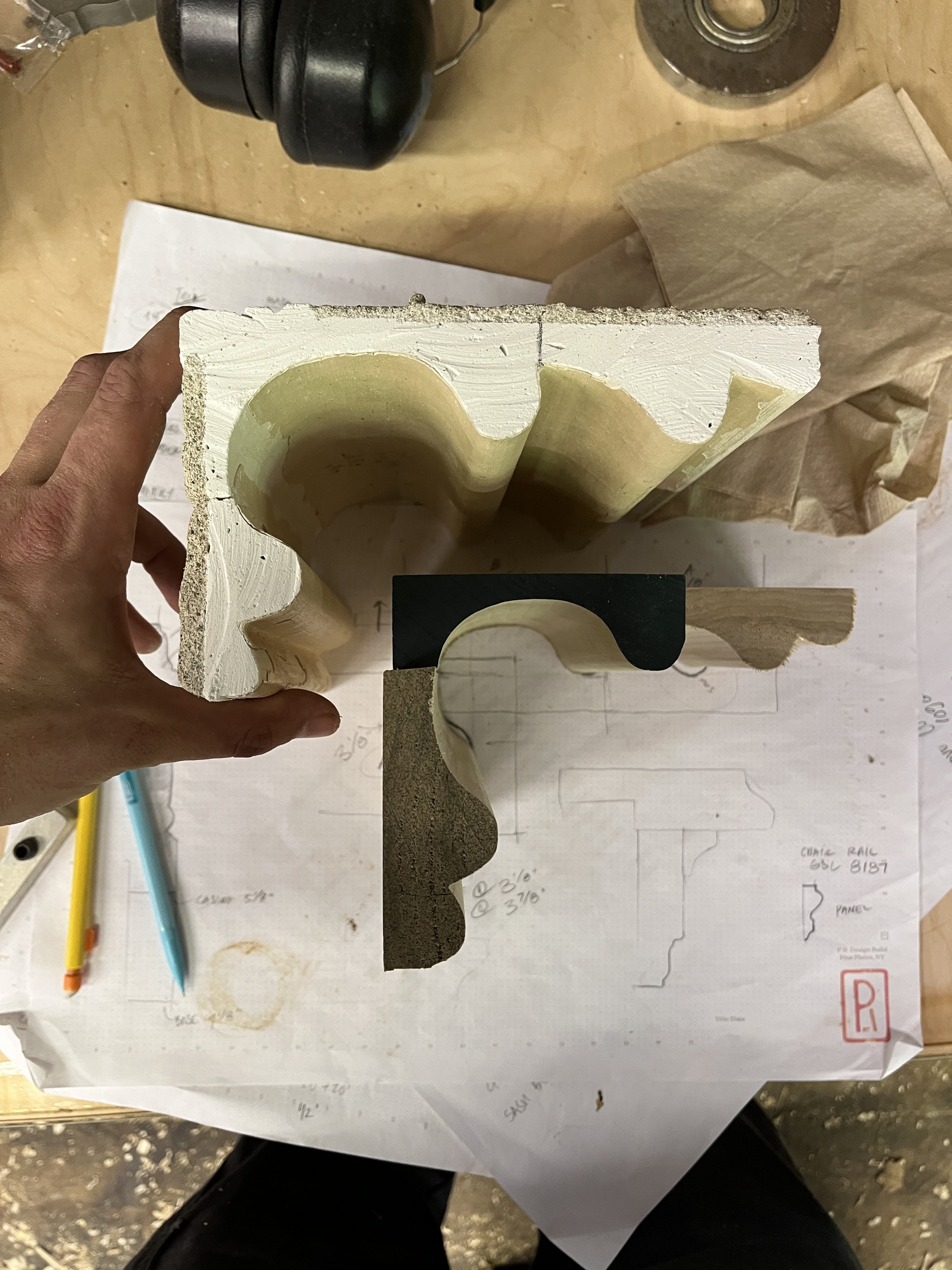 A person holding a custom made piece of moulding next to the existing profile from an old house. Matching the existing profile to reproduce historic trim.