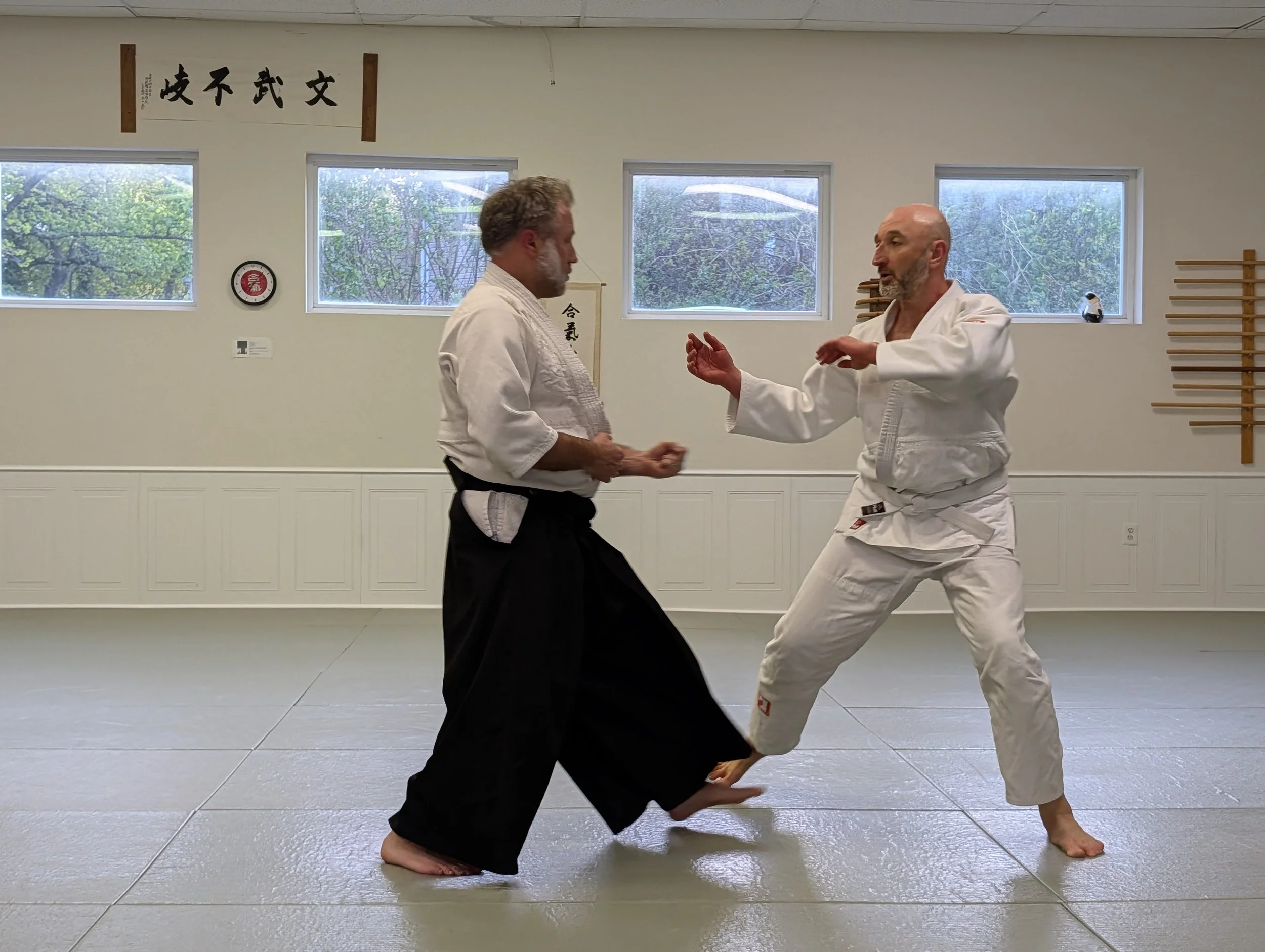 Two men practicing martial arts in a dojo, with one man acting as uke, preparing to punch the nage during practice.