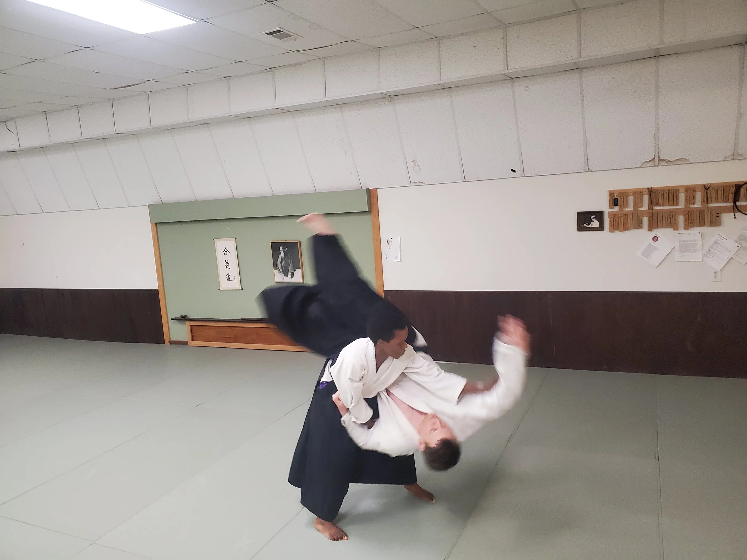 Two martial artists practicing Aikido at the Aikido of Norfolk's dojo; the student is throwing Assistant Instructor Eric Pierce in a koshi nage.