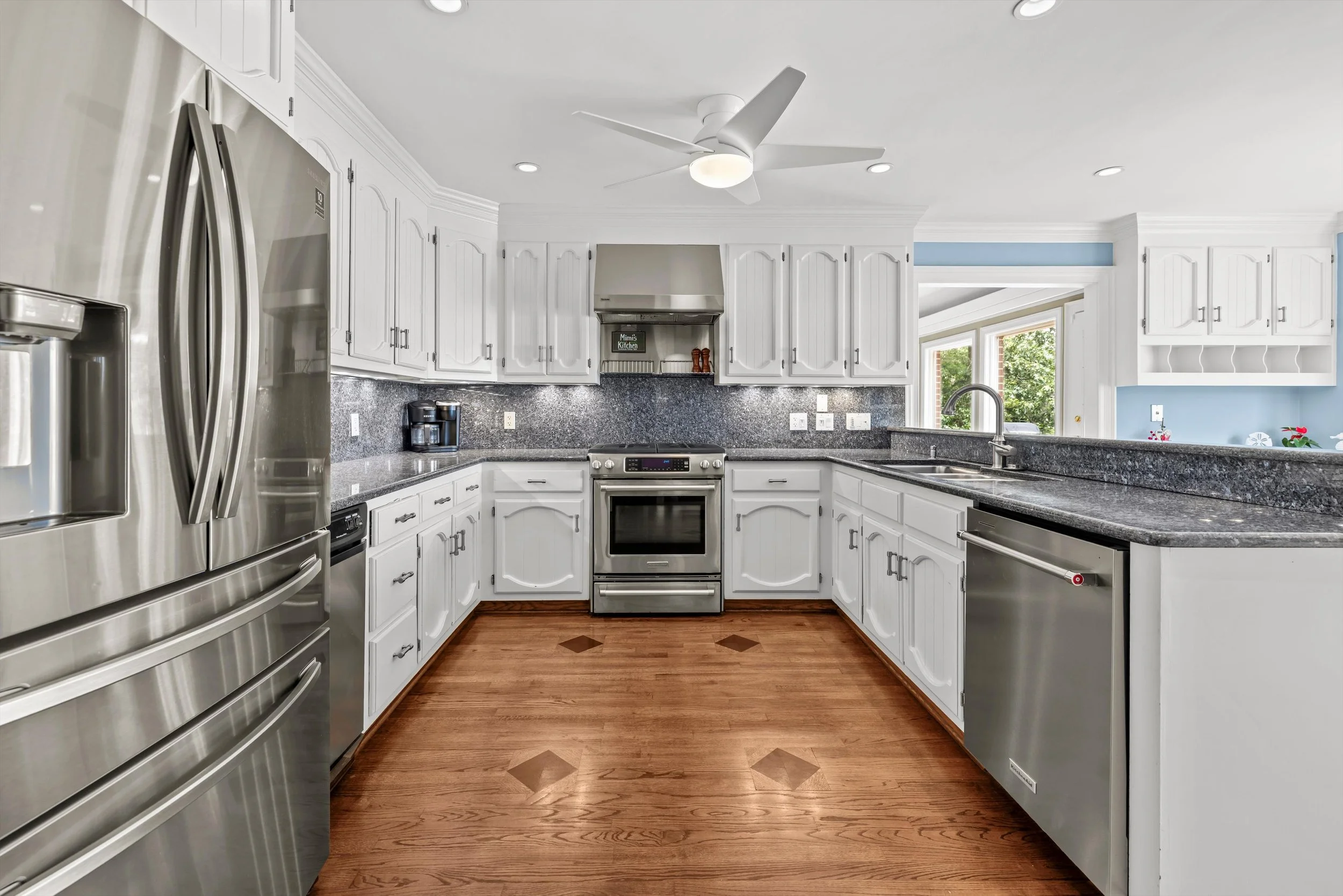 Kitchen with white cabinets, stainless steel appliances, granite countertops, hardwood floor, and a ceiling fan.