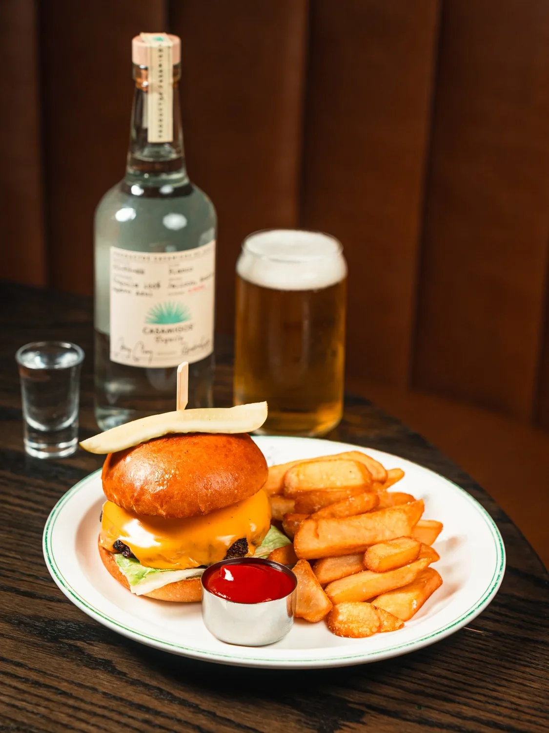 A bottle of tequila, a shot glass and a pint of beer beside a burger at The Fortunate Fox