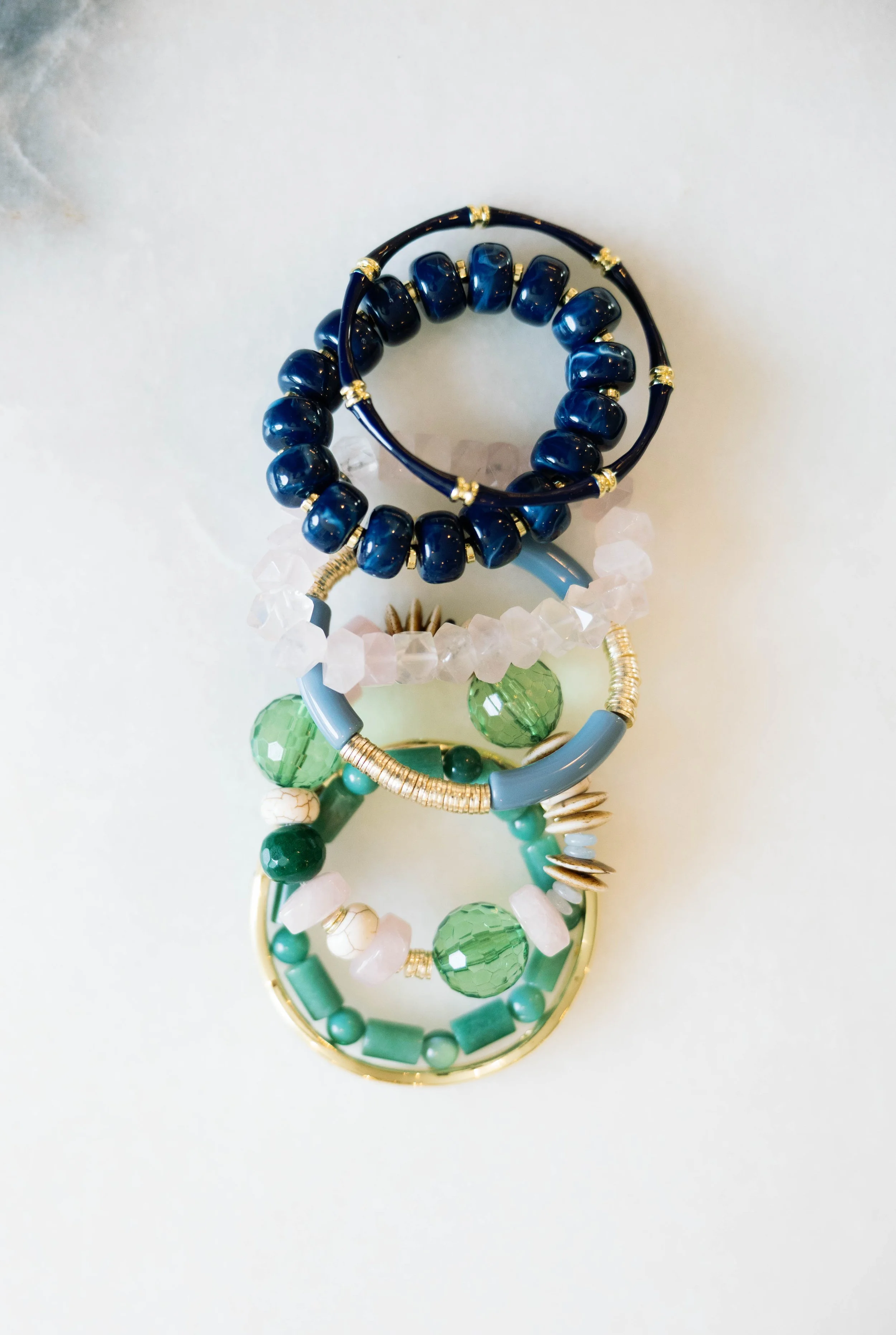 Multiple colorful beaded and metal bangles stacked on a white surface.