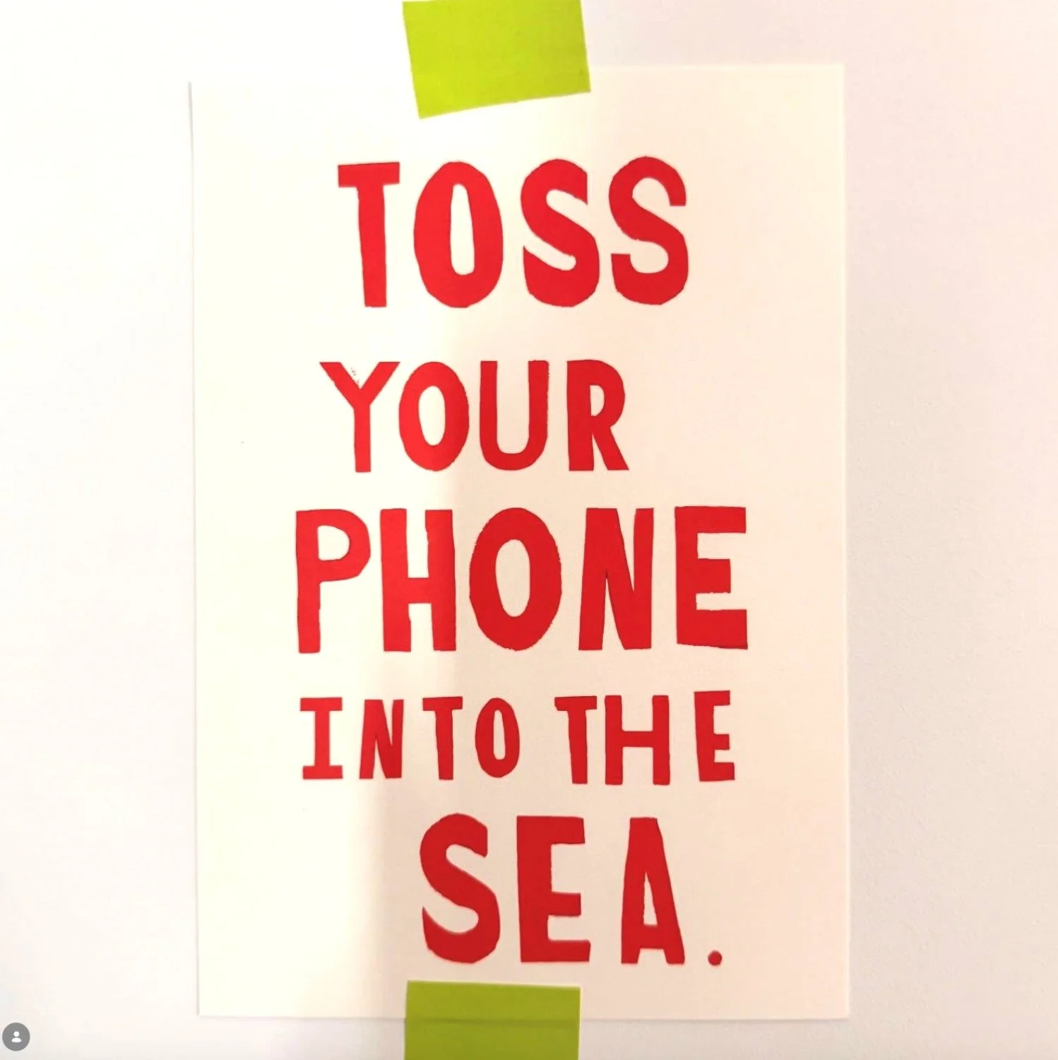 Sign with red text that says 'Toss your phone into the sea' taped to a white wall.