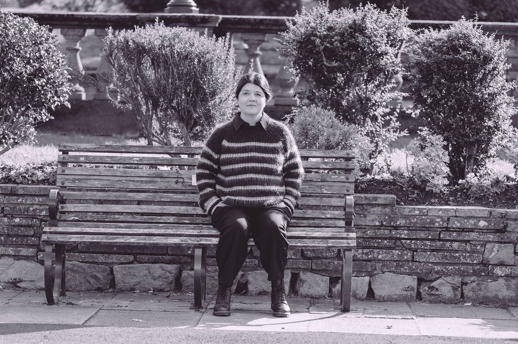 Photo of therapist sitting on a bench in Southport marine lake wearing a striped jumper and trousers