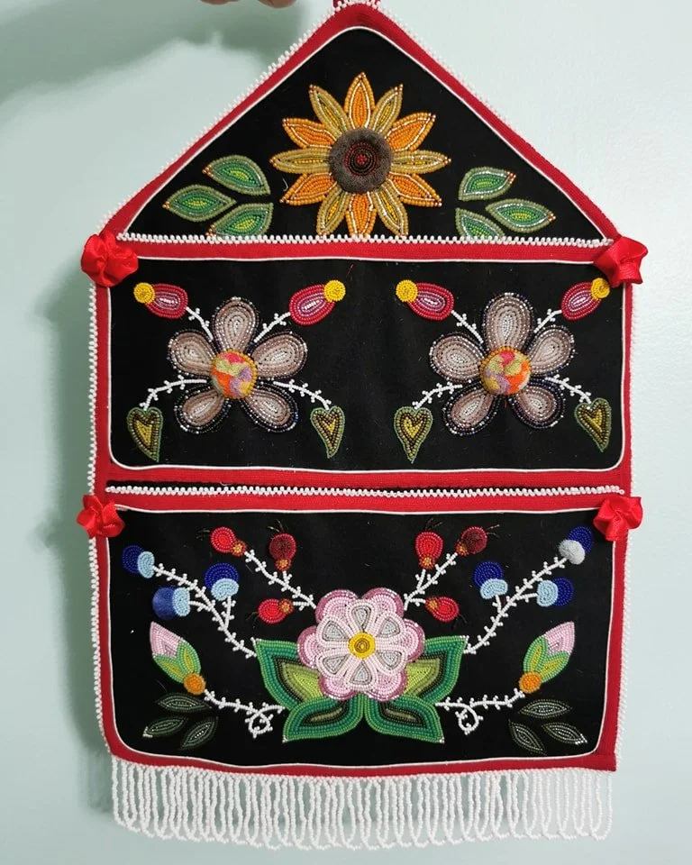Beaded wall hanging with floral designs on a black background, featuring colorful flowers, leaves, and decorative elements.