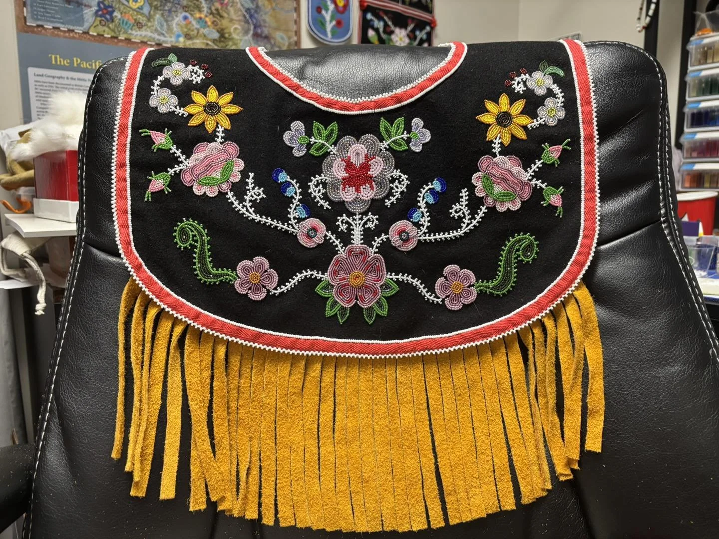 Black leather chair decorated with a colorful beaded yoke with leather fringe. The embroidery features floral patterns in pink, yellow, green, blue, and white.