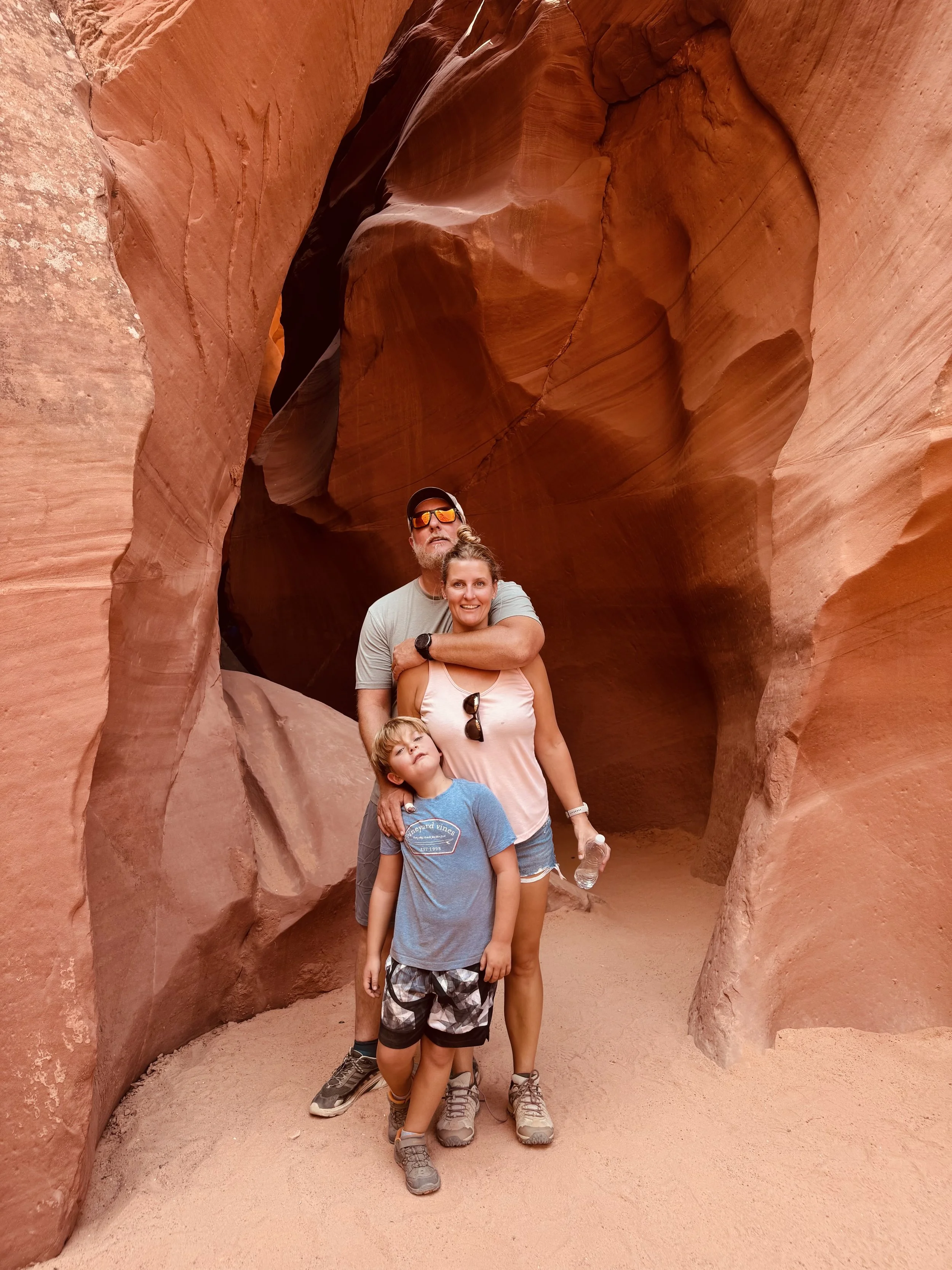 A family of four standing inside a narrow, winding slot canyon with smooth, orange-red sandstone walls.