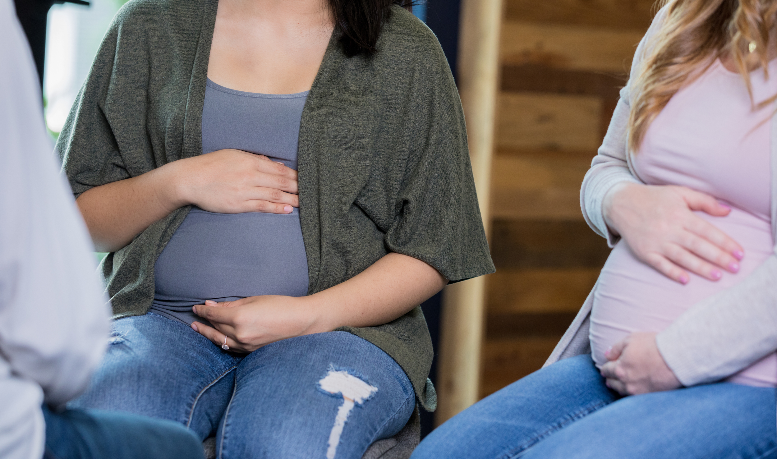 Group of women sitting close together, with their hands over their stomachs, possibly during a support group or discussion session.
