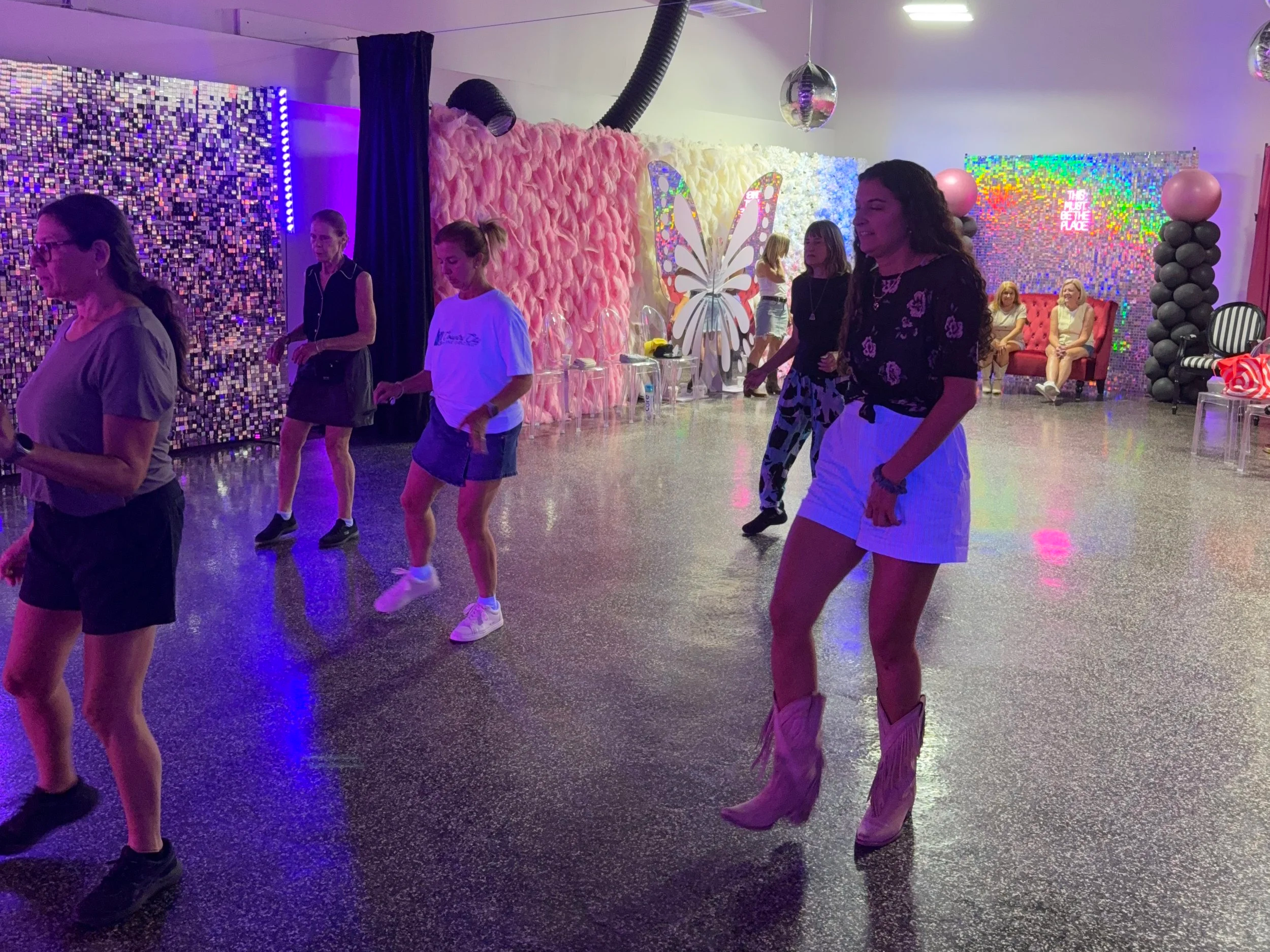 People dancing and socializing in a colorful, vibrant indoor space with decorated walls, balloons, and neon signs.