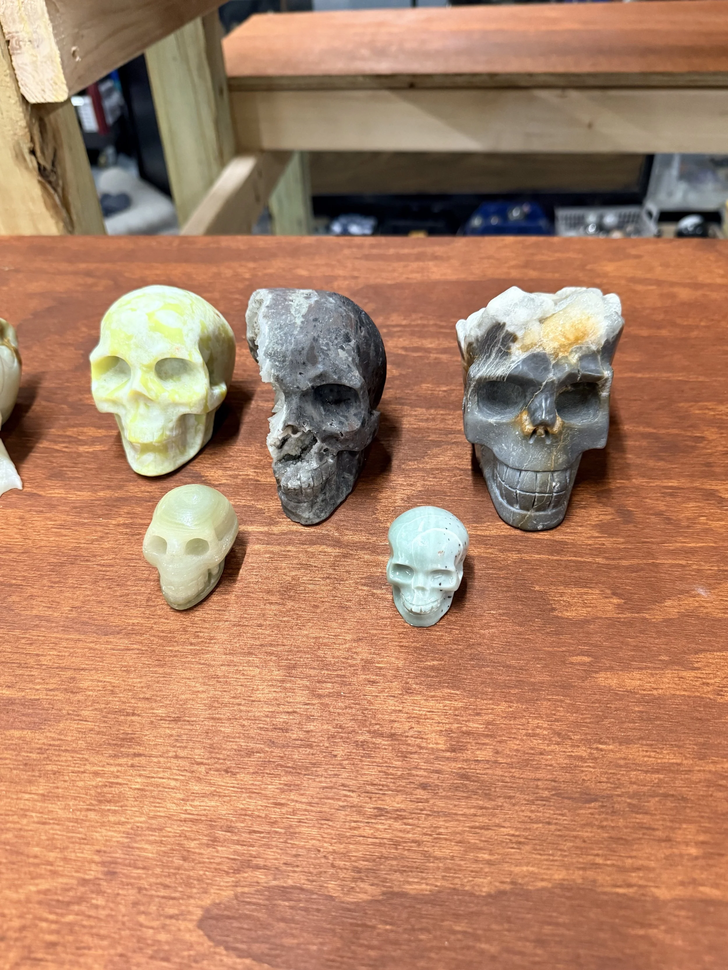 A row of carved skull-shaped objects made from various types of stone or minerals, displayed on a wooden surface.