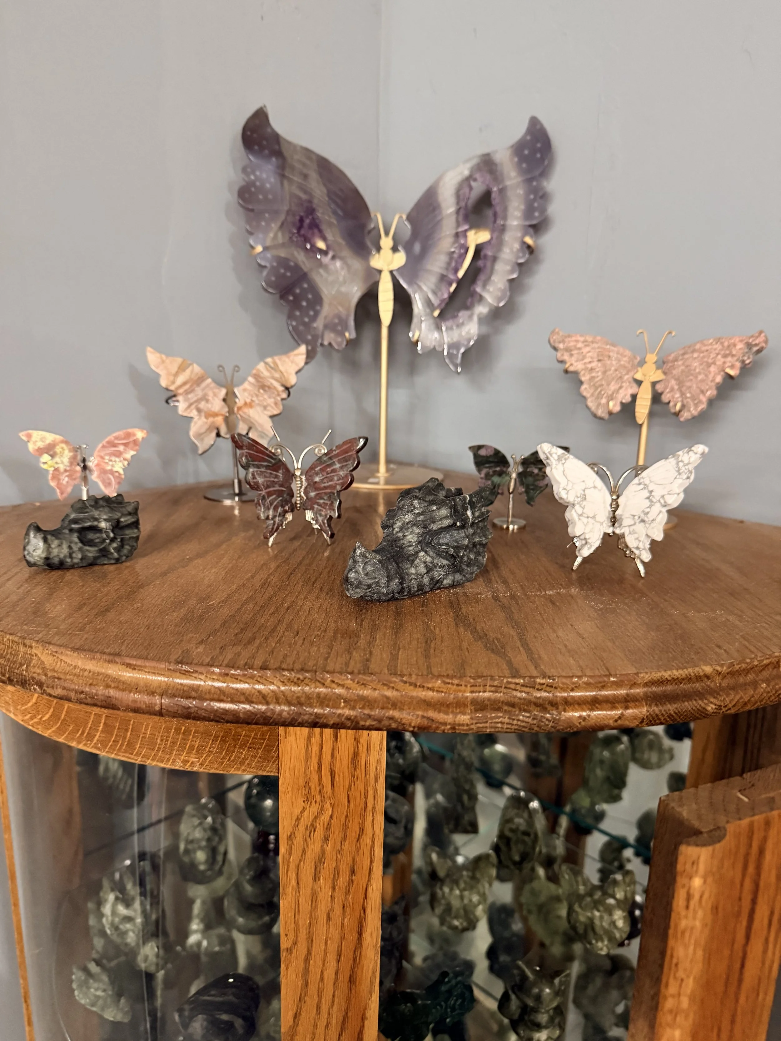 Collection of decorative butterfly figurines displayed on a wooden table with rocks.