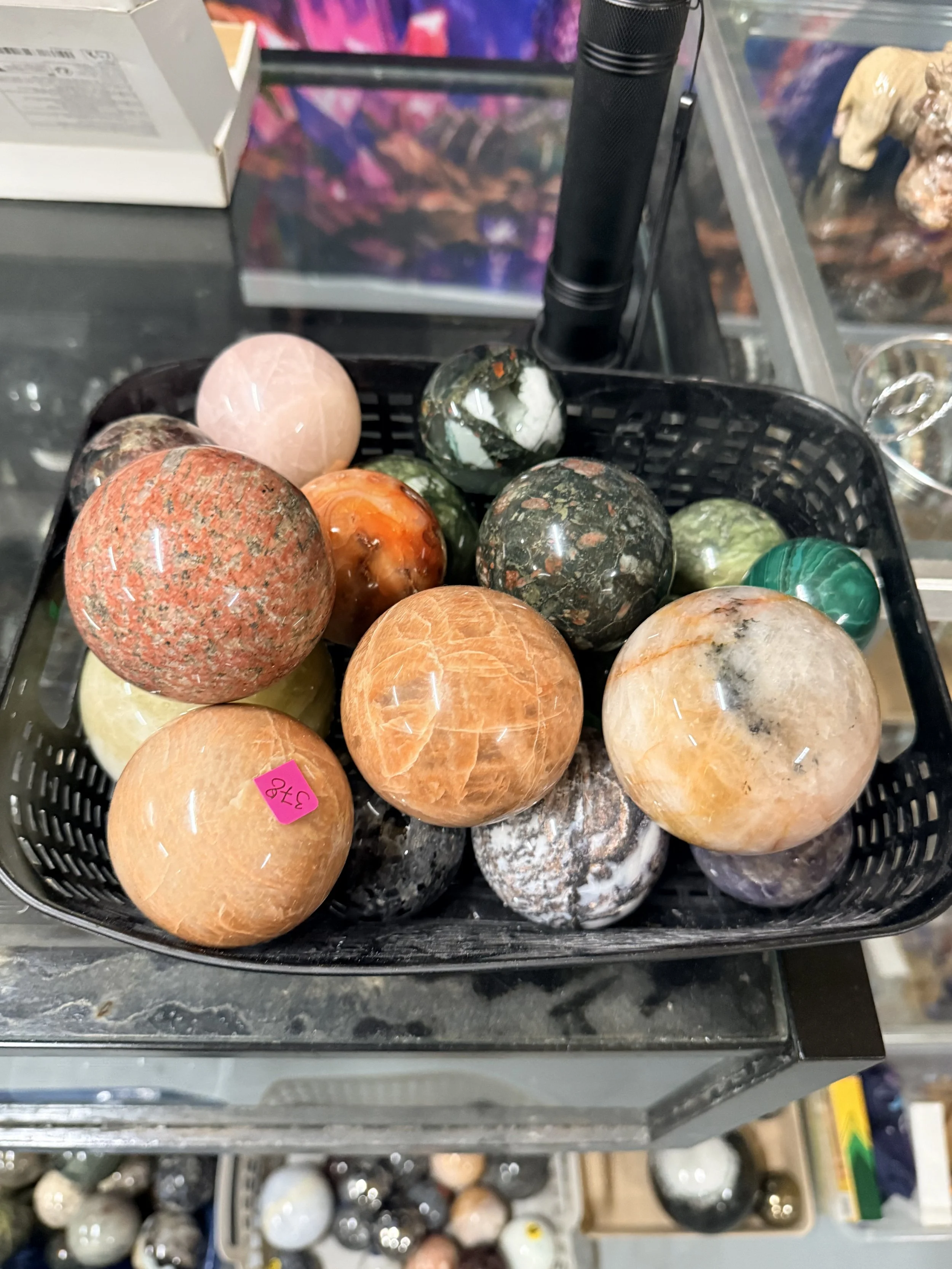 Various polished marble spheres displayed in a black plastic basket on a store shelf.