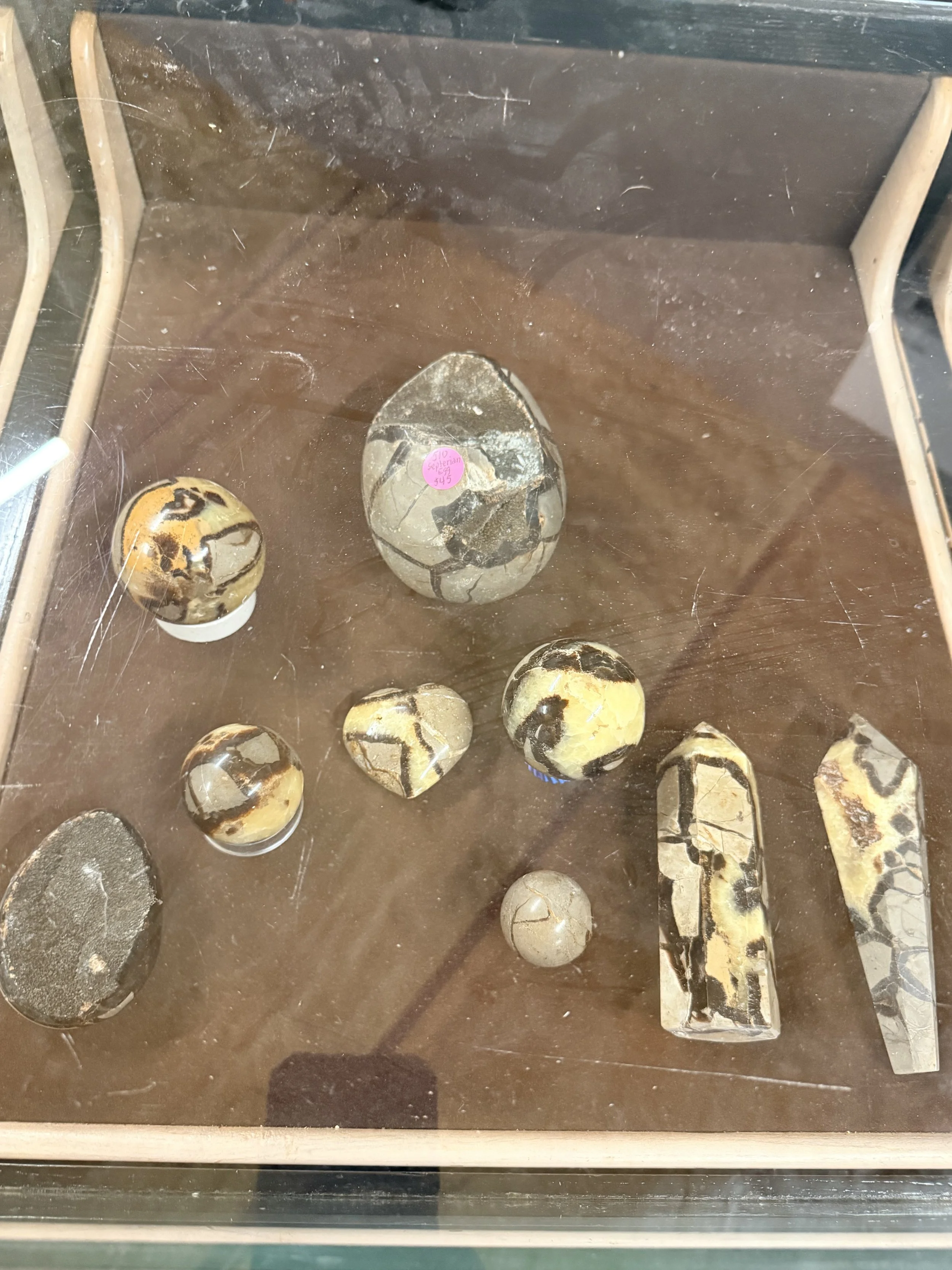Collection of polished stones and rocks displayed inside a glass case, with some stones having a marbled appearance and others with crackling patterns.