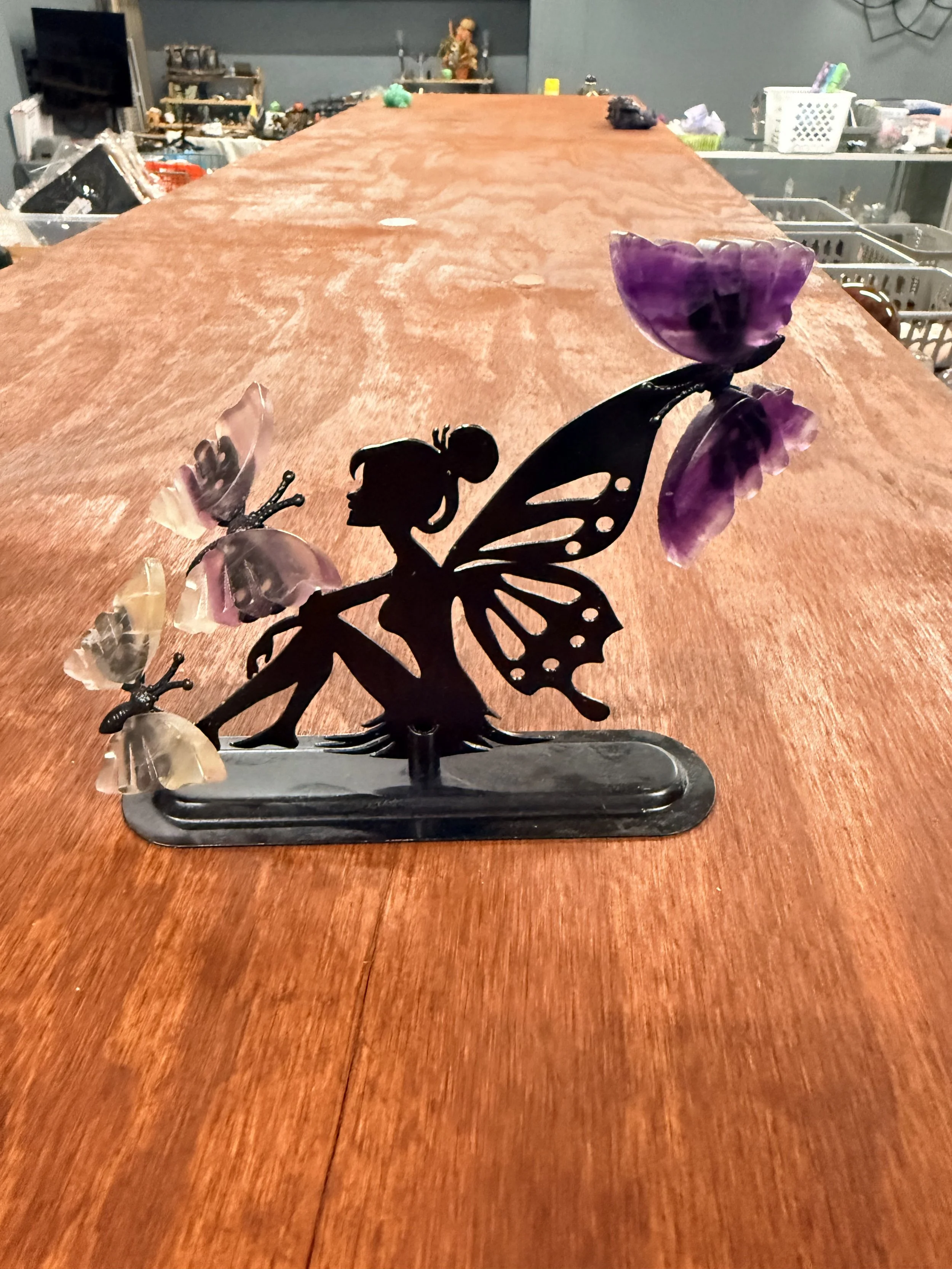 Decorative metal fairy silhouette with purple and pink glass flowers on a wooden surface.