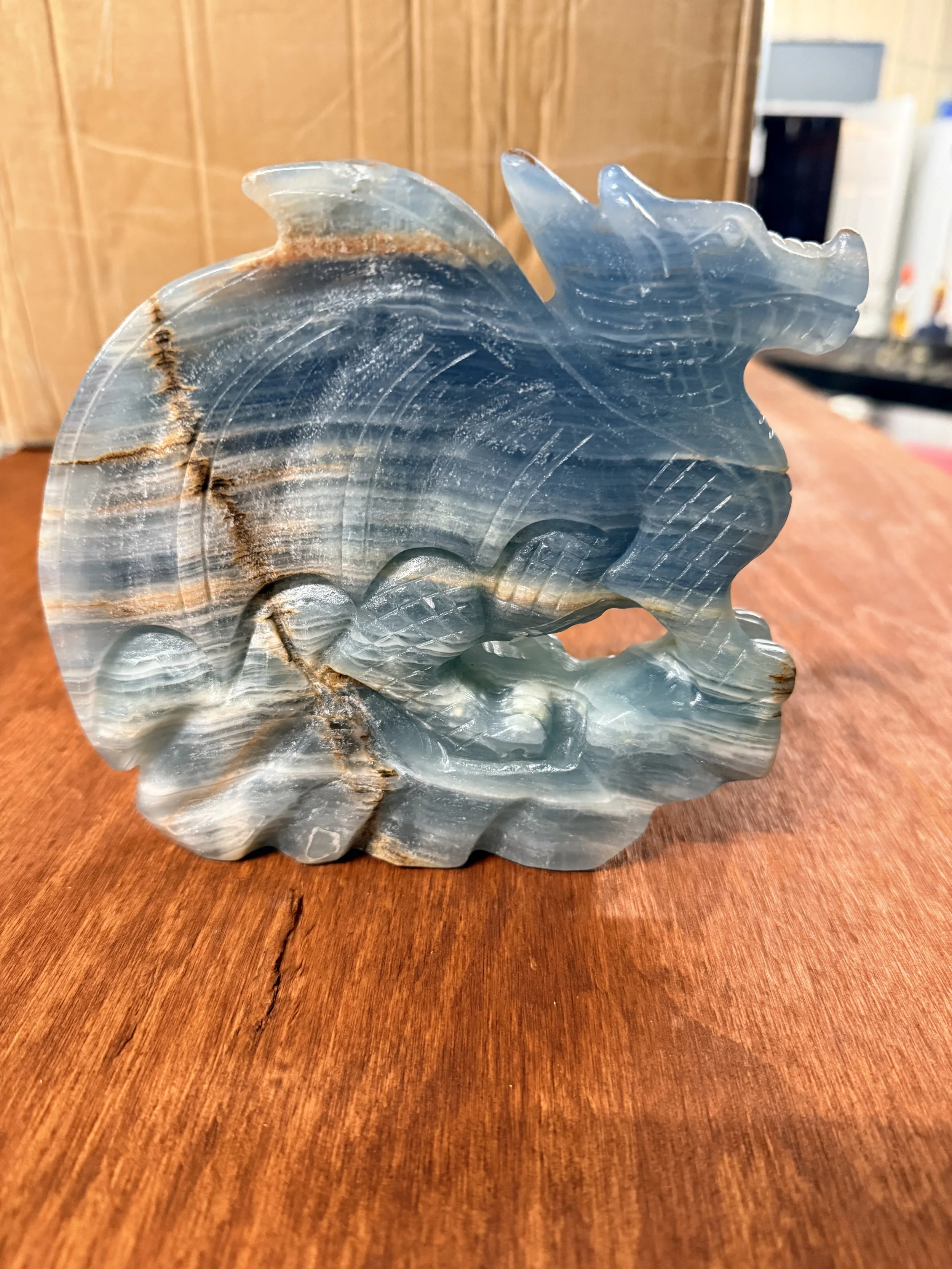 Close-up of a carved blue and gray onyx or marble sculpture resembling a stylized fish or dragon, resting on a wooden surface with a blurred background.