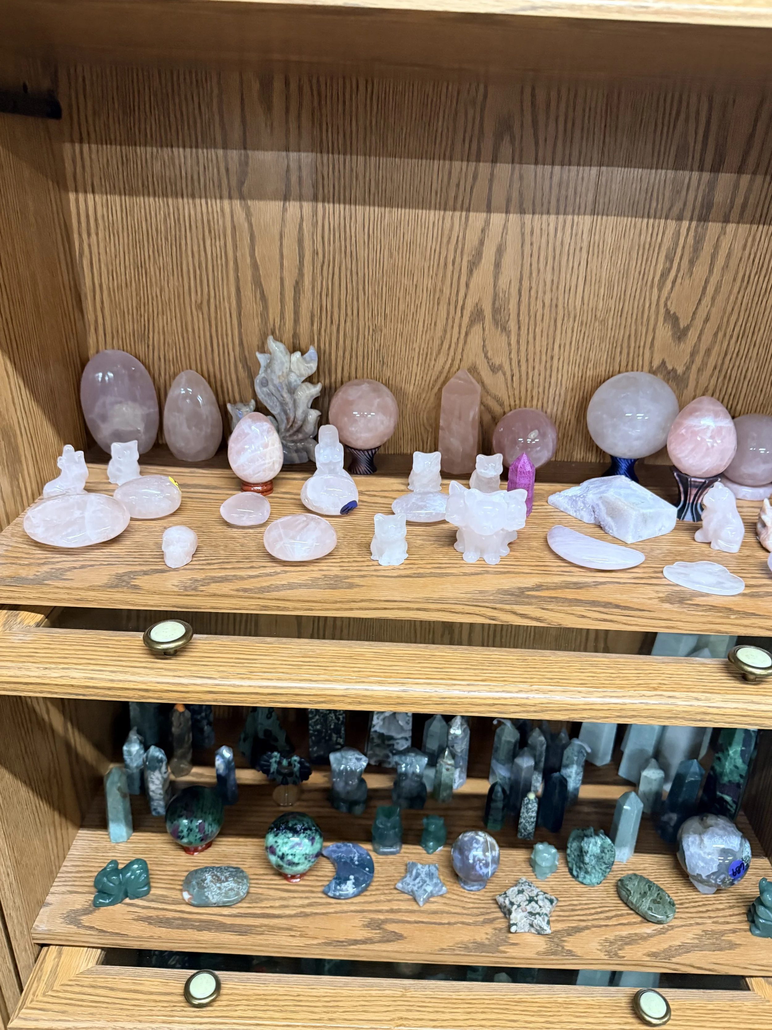 Display shelf containing various polished and raw gemstones, crystals, and mineral specimens arranged on wooden shelves.