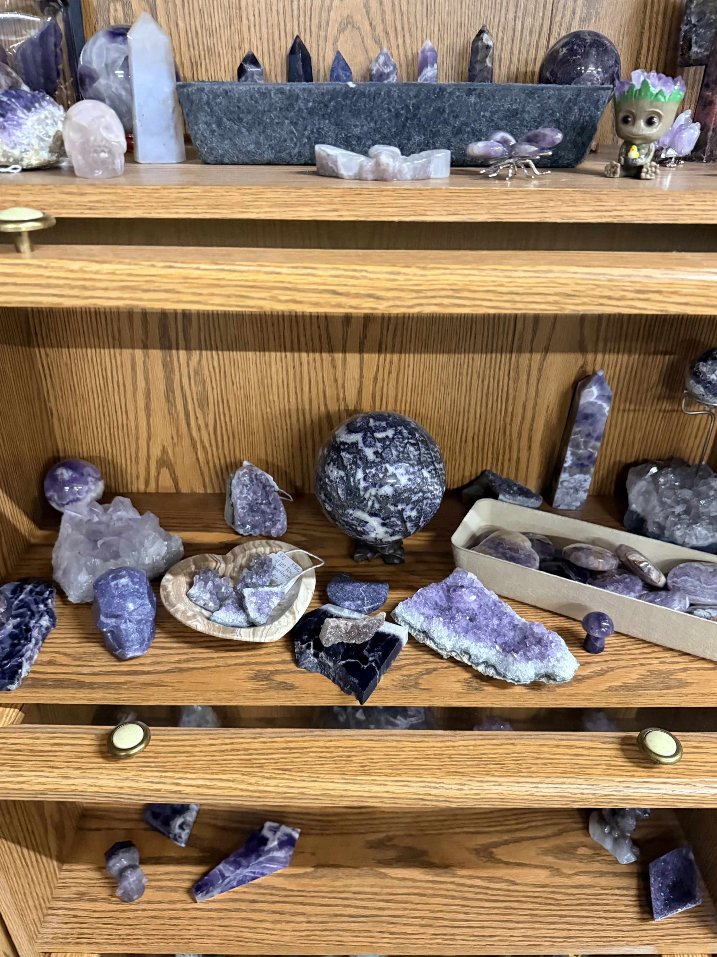 Wooden shelf with various purple and lavender crystals and mineral specimens displayed.