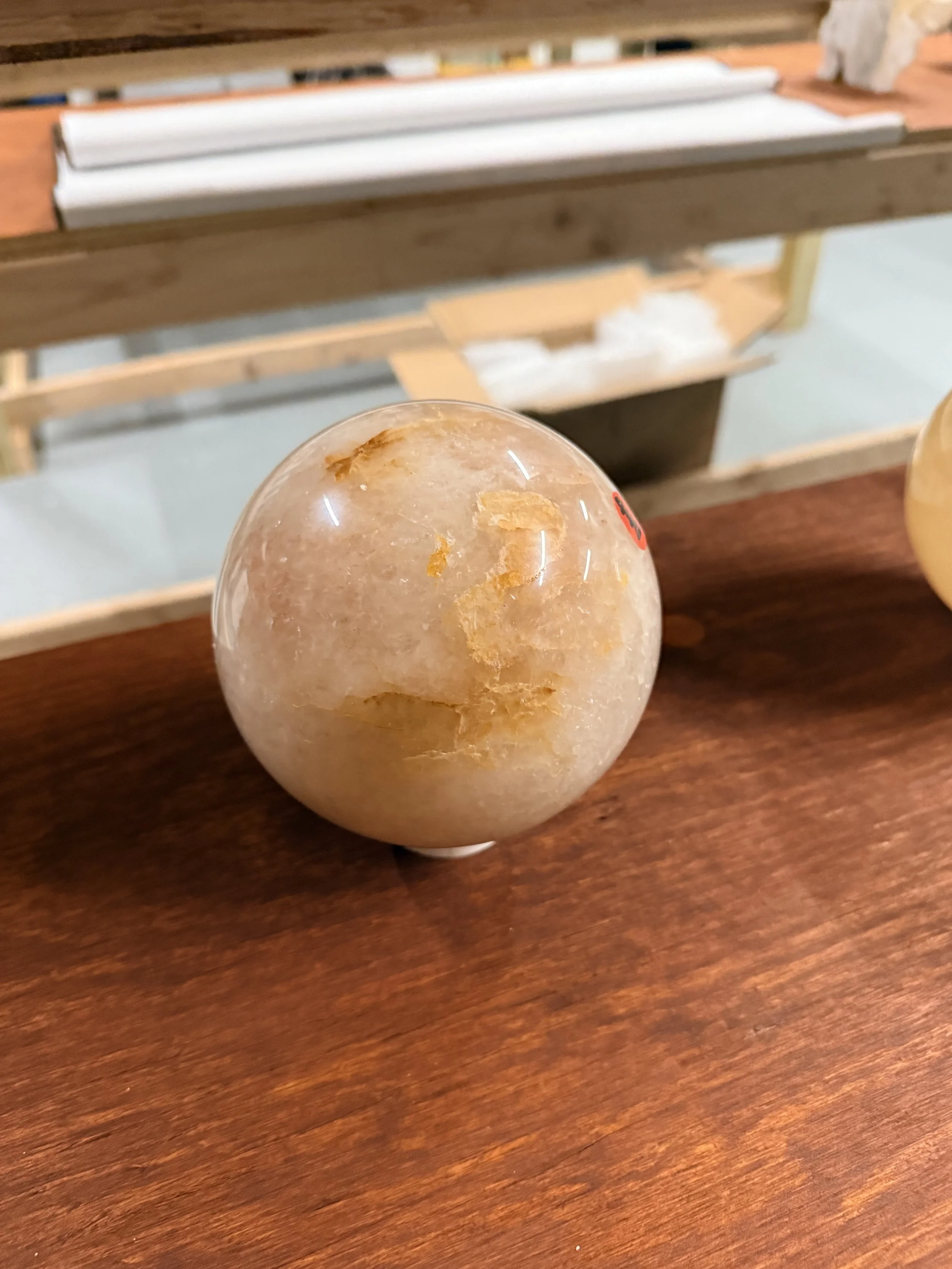 A round, semi-transparent salt lamp with a rough texture and orange streaks, resting on a wooden surface.