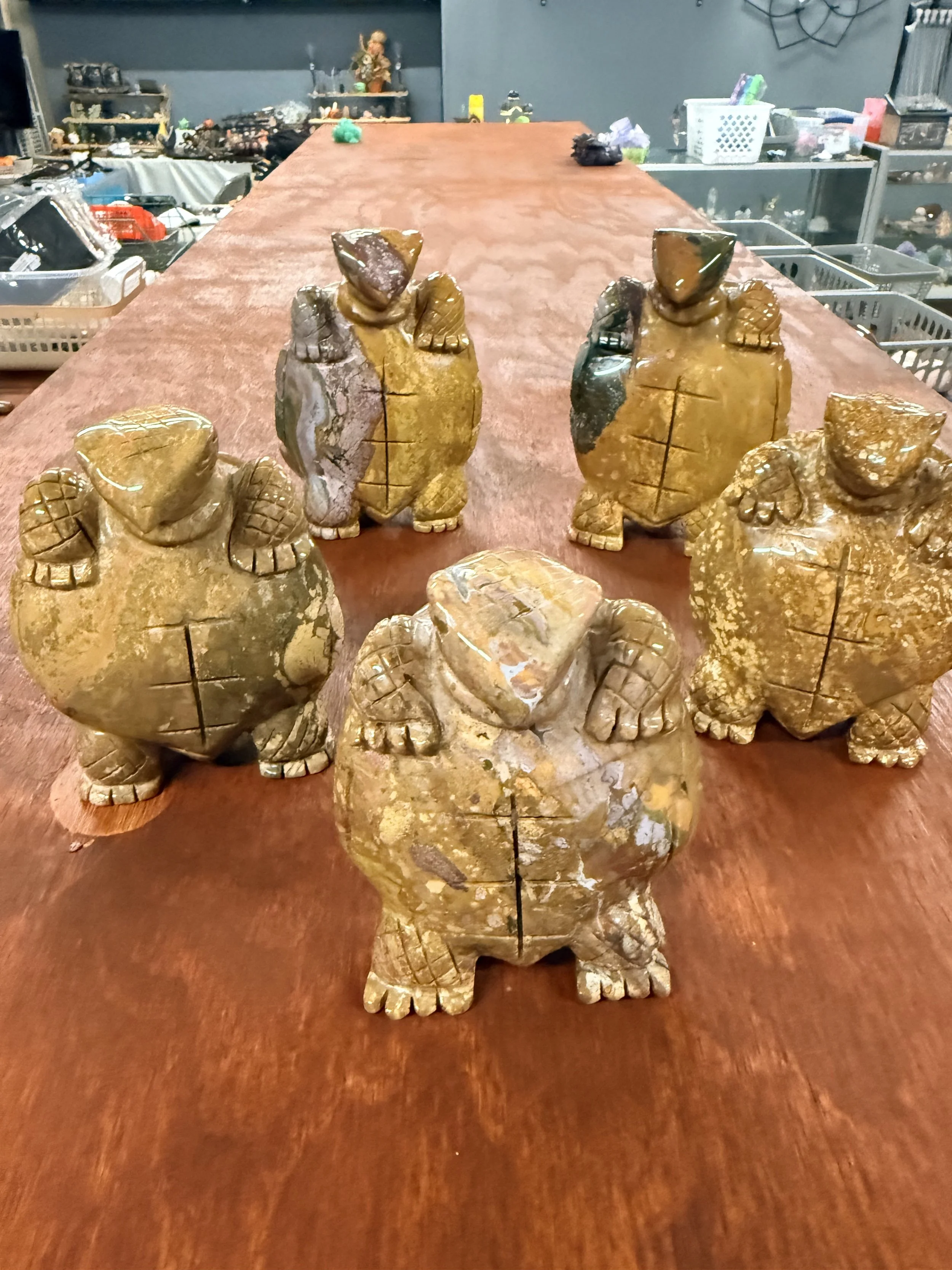 Several carved stones of various sizes and shapes, resembling animals, arranged on a wooden table with a cluttered background of shelves, plastic bins, and miscellaneous items.