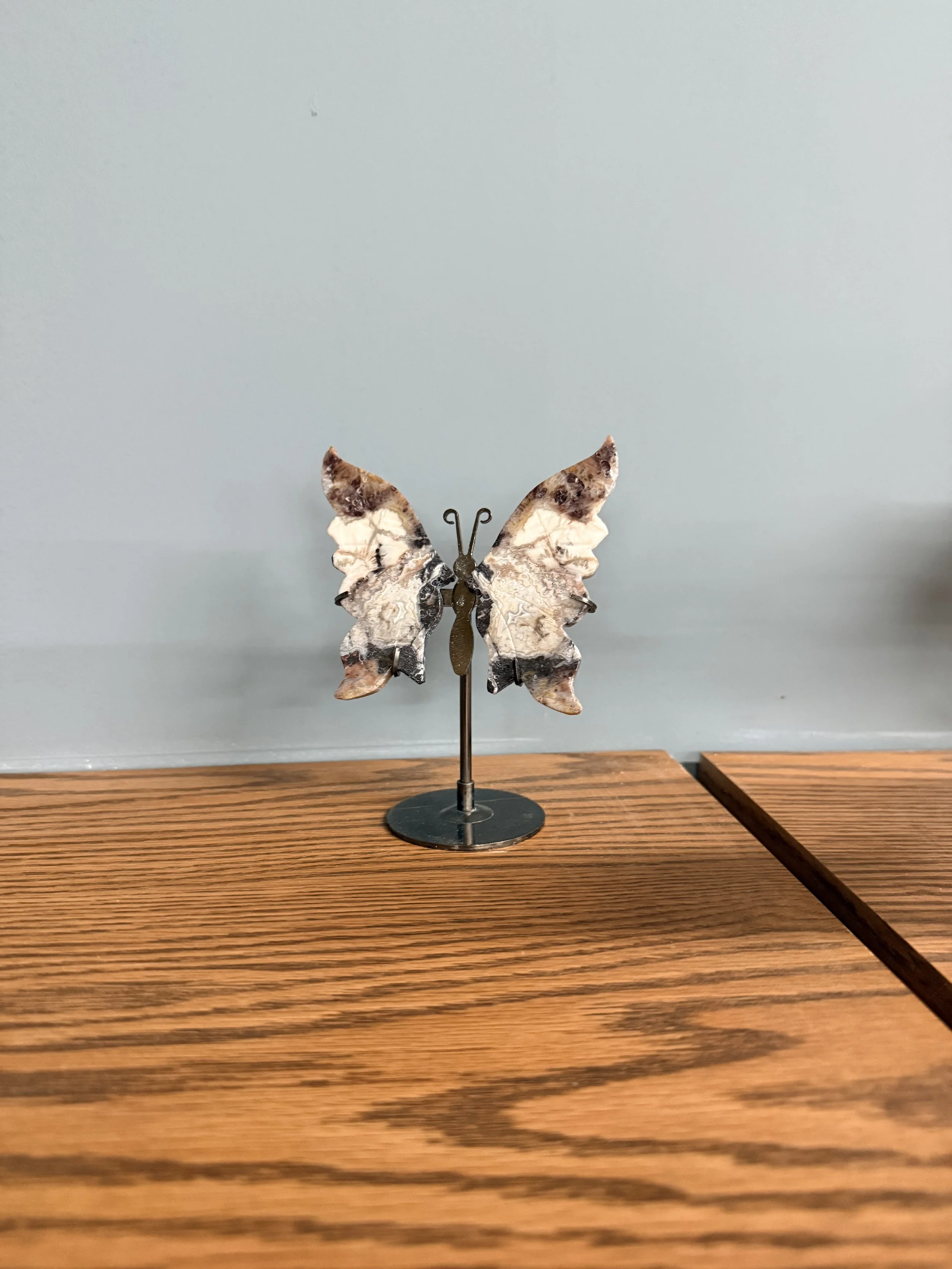 Decorative butterfly sculpture with patterned wings on a stand, placed on a wooden surface.
