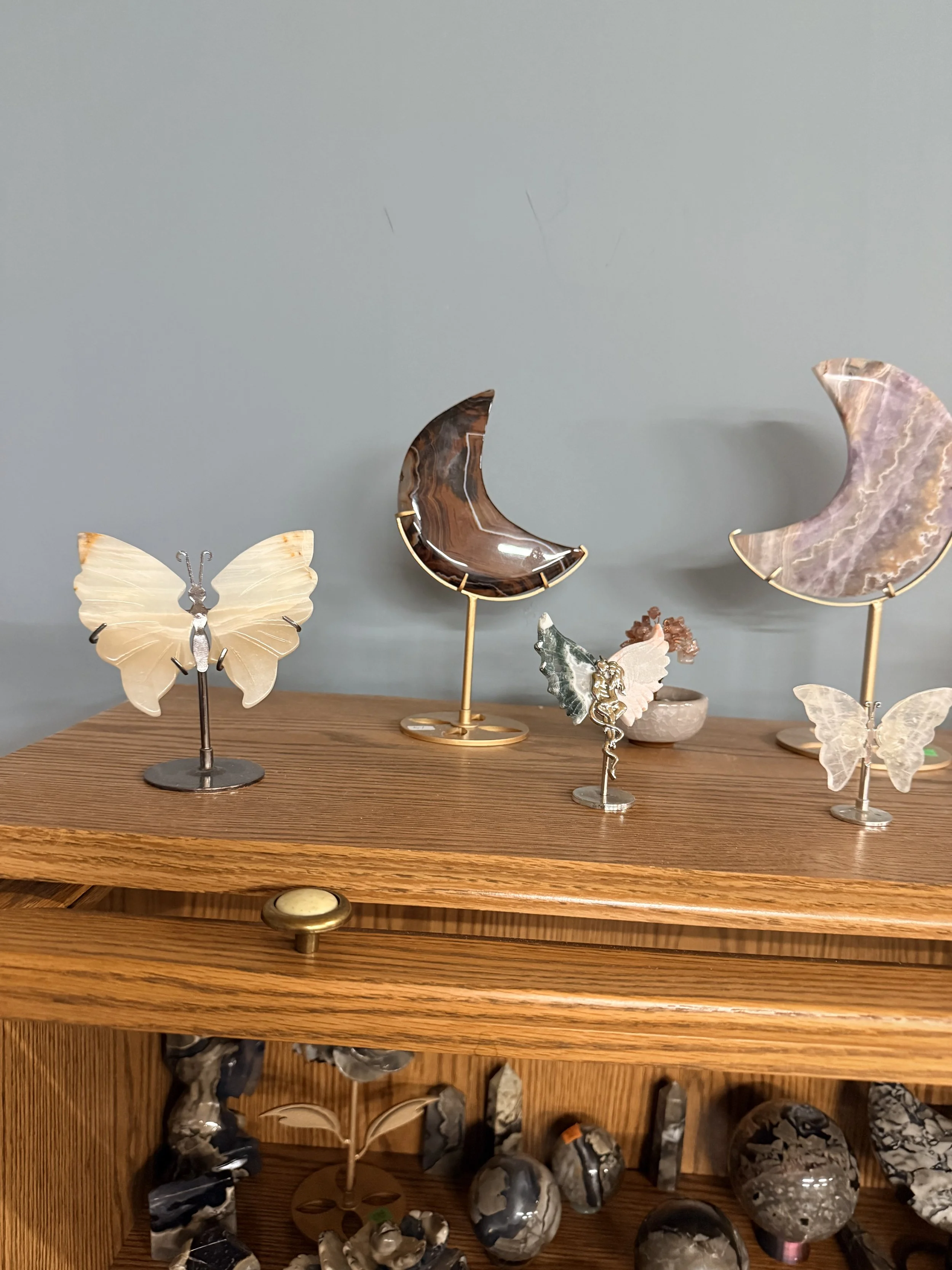 Decorative display featuring marble and onyx moon and butterfly sculptures on a wooden surface with a shelf of various stones below.