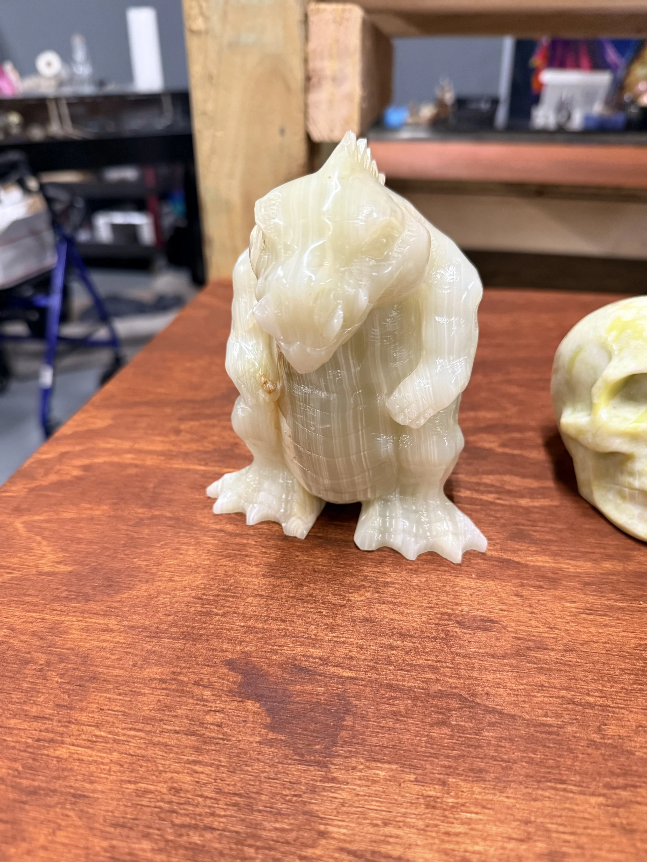 A large, cream-colored, and intricately carved seashell with a textured surface, placed on a wooden table with a reddish-brown finish. In the background, there's a blurred view of a workshop or garage with shelves, tools, and miscellaneous items.