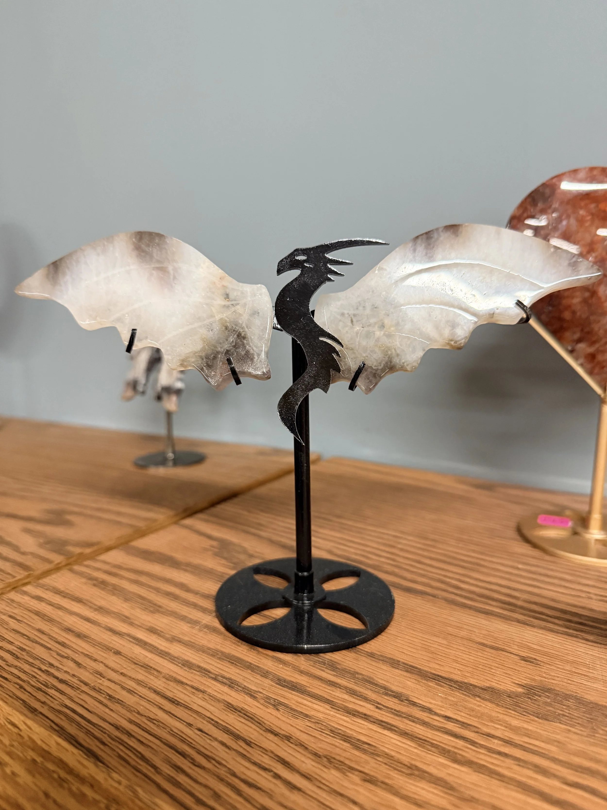A decorative butterfly-shaped object made of translucent material with a black metal seahorse in the center, mounted on a black stand, displayed on a wooden surface.