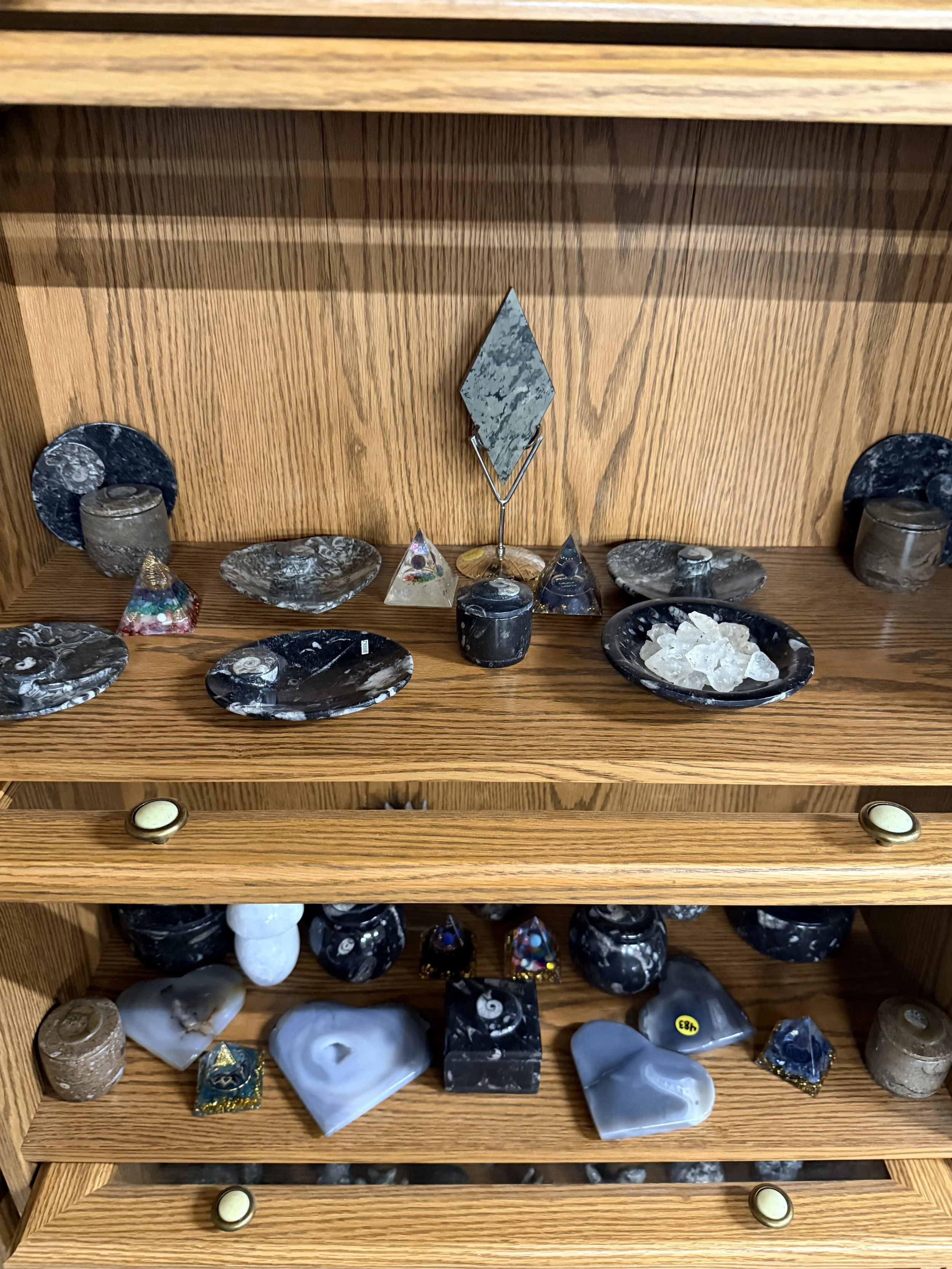 Display shelf filled with various mineral and gemstone specimens of different shapes, sizes, and colors, with some polished and some raw.