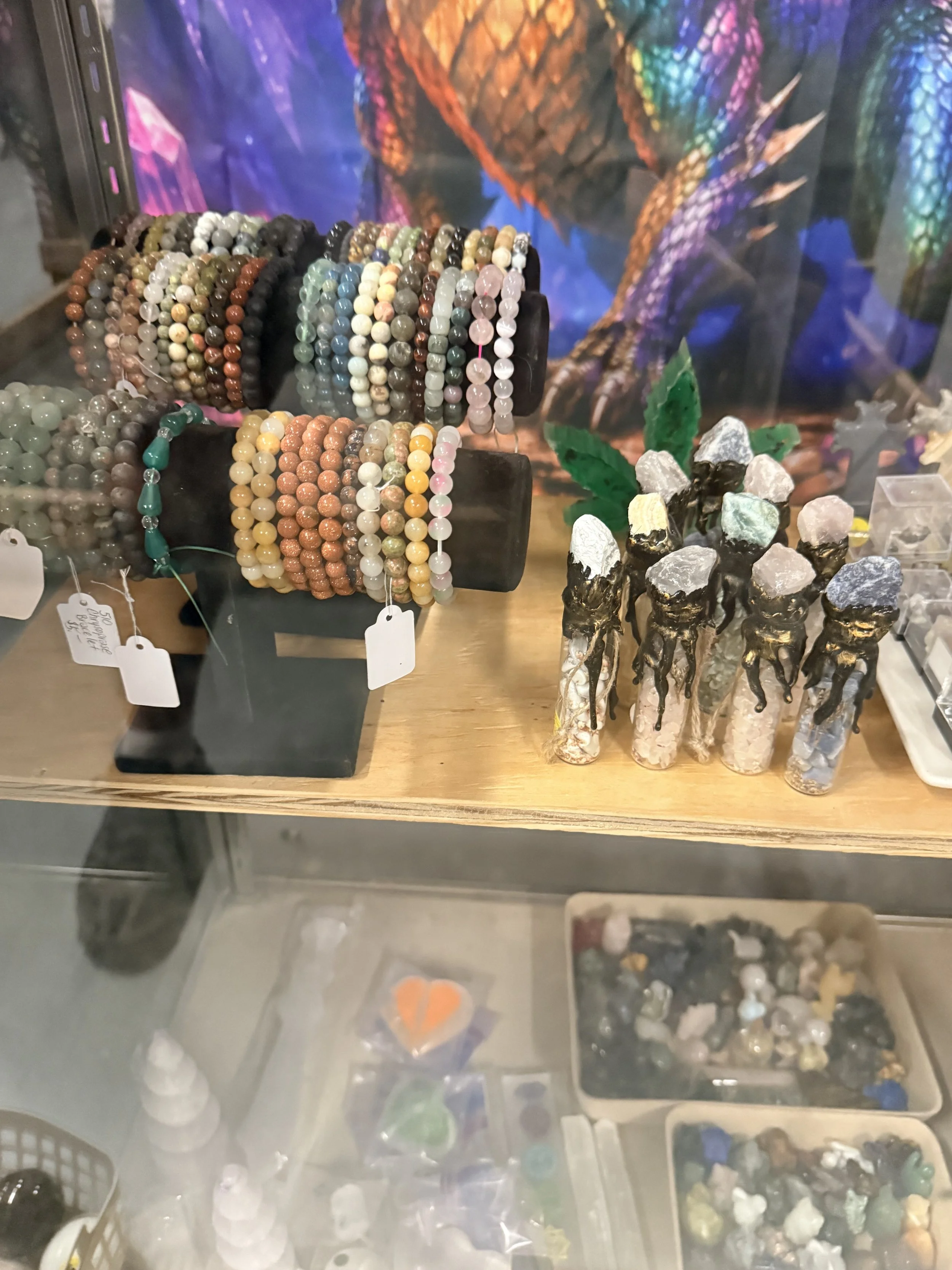 Display case with various beaded bracelets and jewelry, along with decorative rocks and minerals on a wooden surface.