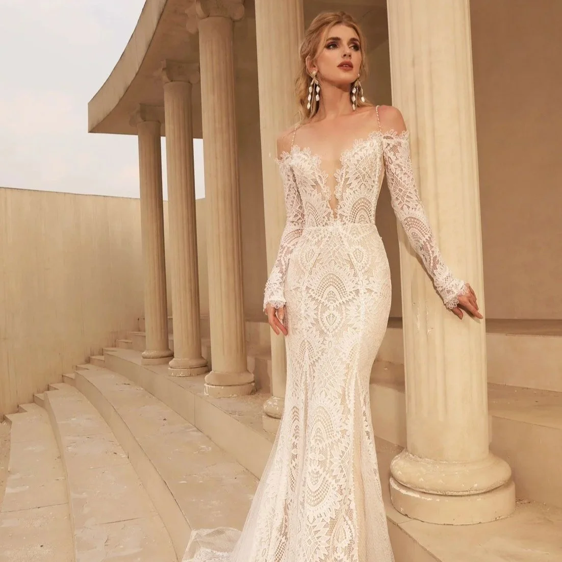 A woman in a long, white, lacy wedding dress standing by classical columns and stairs