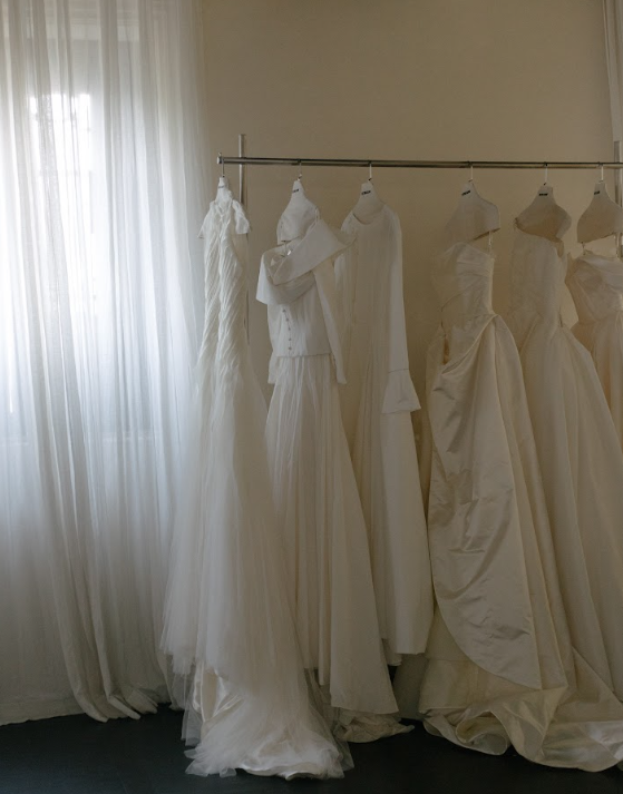 Elegant white wedding dresses hanging on a clothing rack in a softly lit room with sheer curtains.