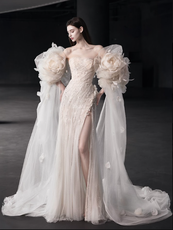Woman wearing an elegant, strapless cream-colored gown with large floral tulle sleeves and a high slit.