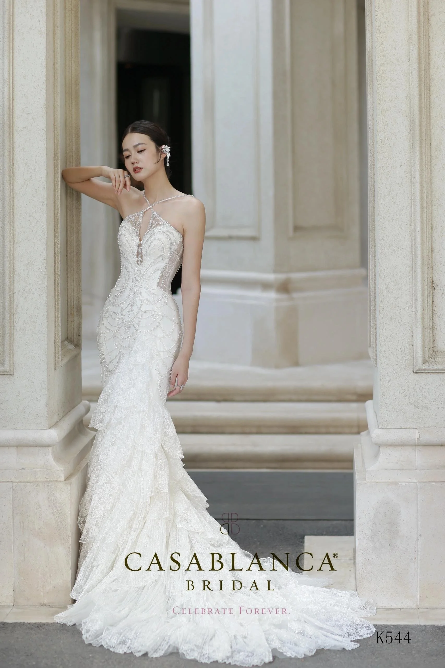 Woman in a white lace wedding dress standing outside near a building.