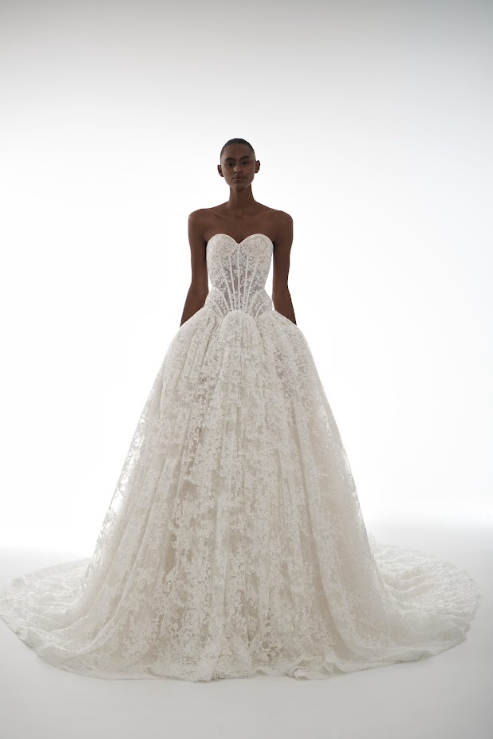 A model wearing a strapless white wedding gown with a fitted bodice and a full, flowing skirt, standing against a plain white background.